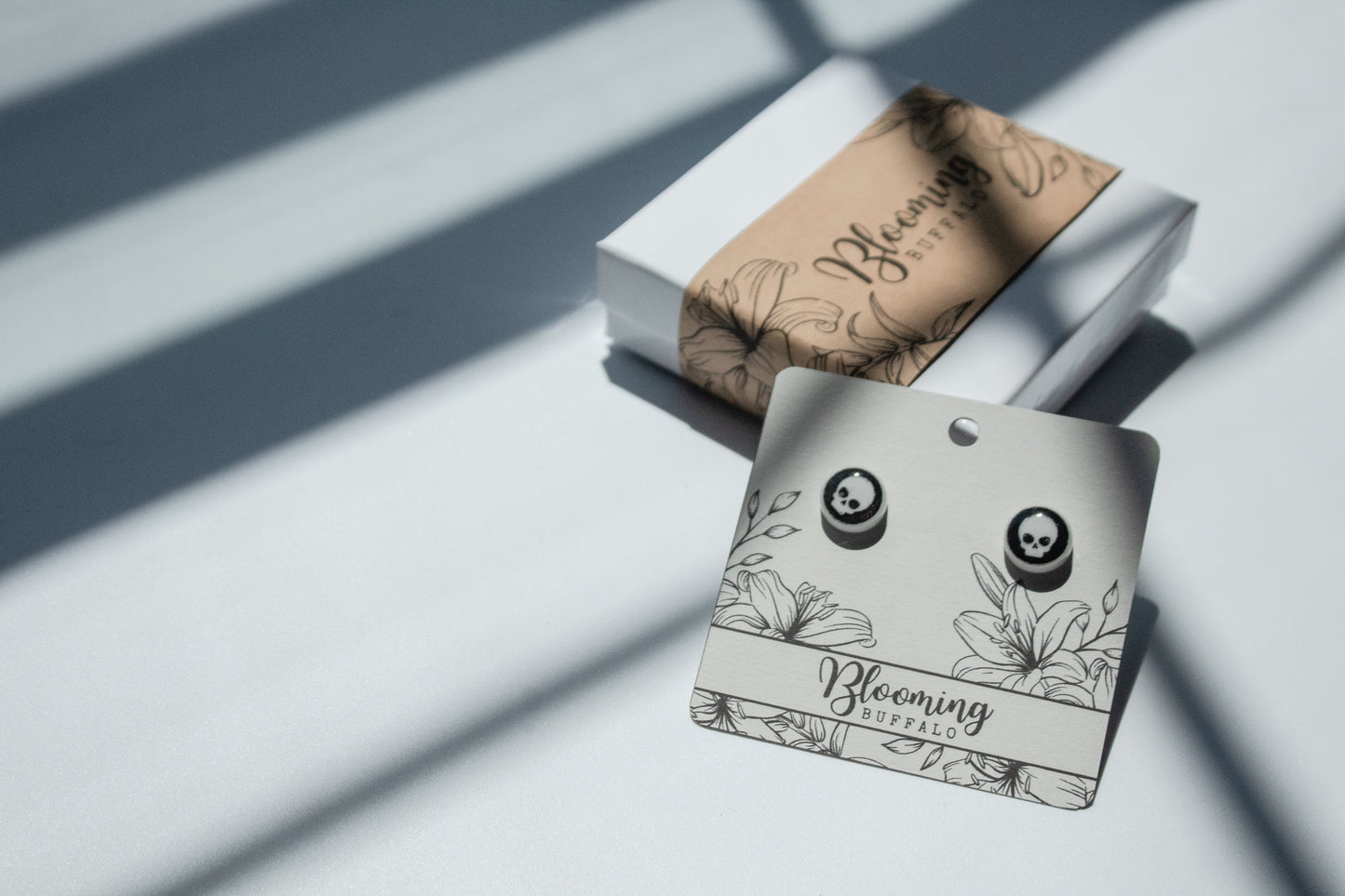white circle stud earrings with a black background and white skull design on a Blooming Buffalo branded earring card and gift box.