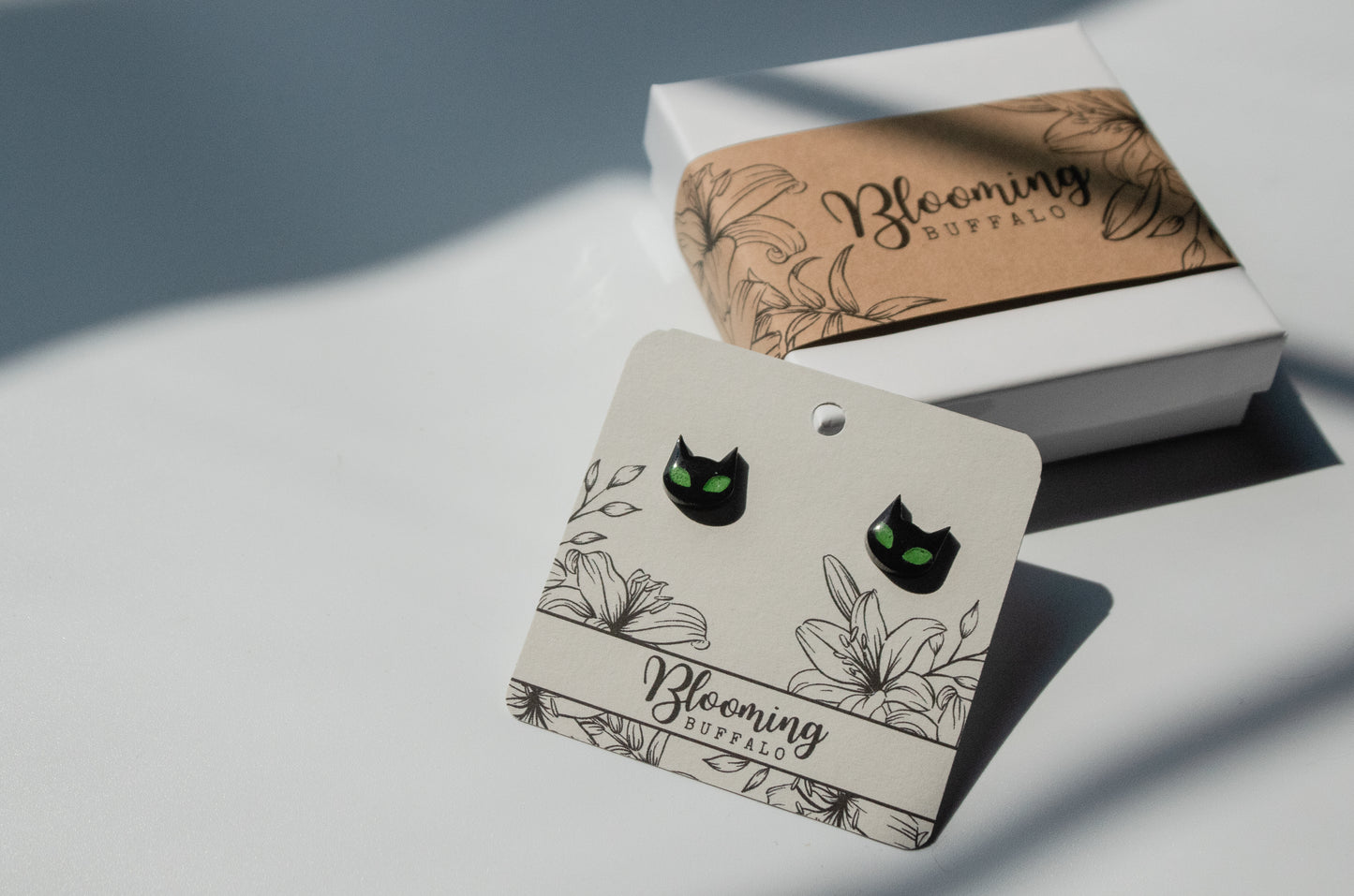 spooky black cat stud earrings with vibrant green eyes on Blooming Buffalo branded earring card