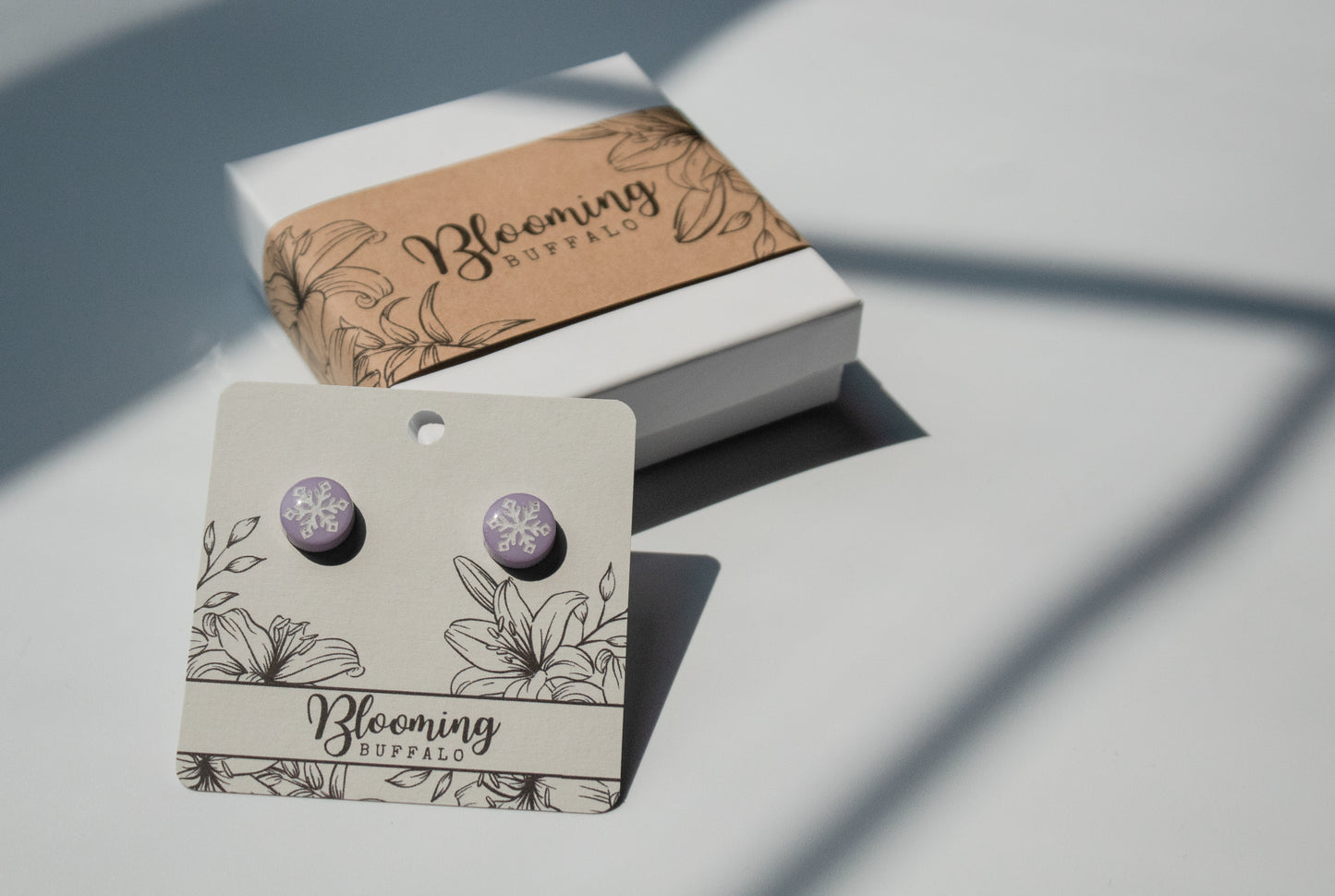 light purple circular studs with white snowflake design on Blooming Buffalo branded earring card