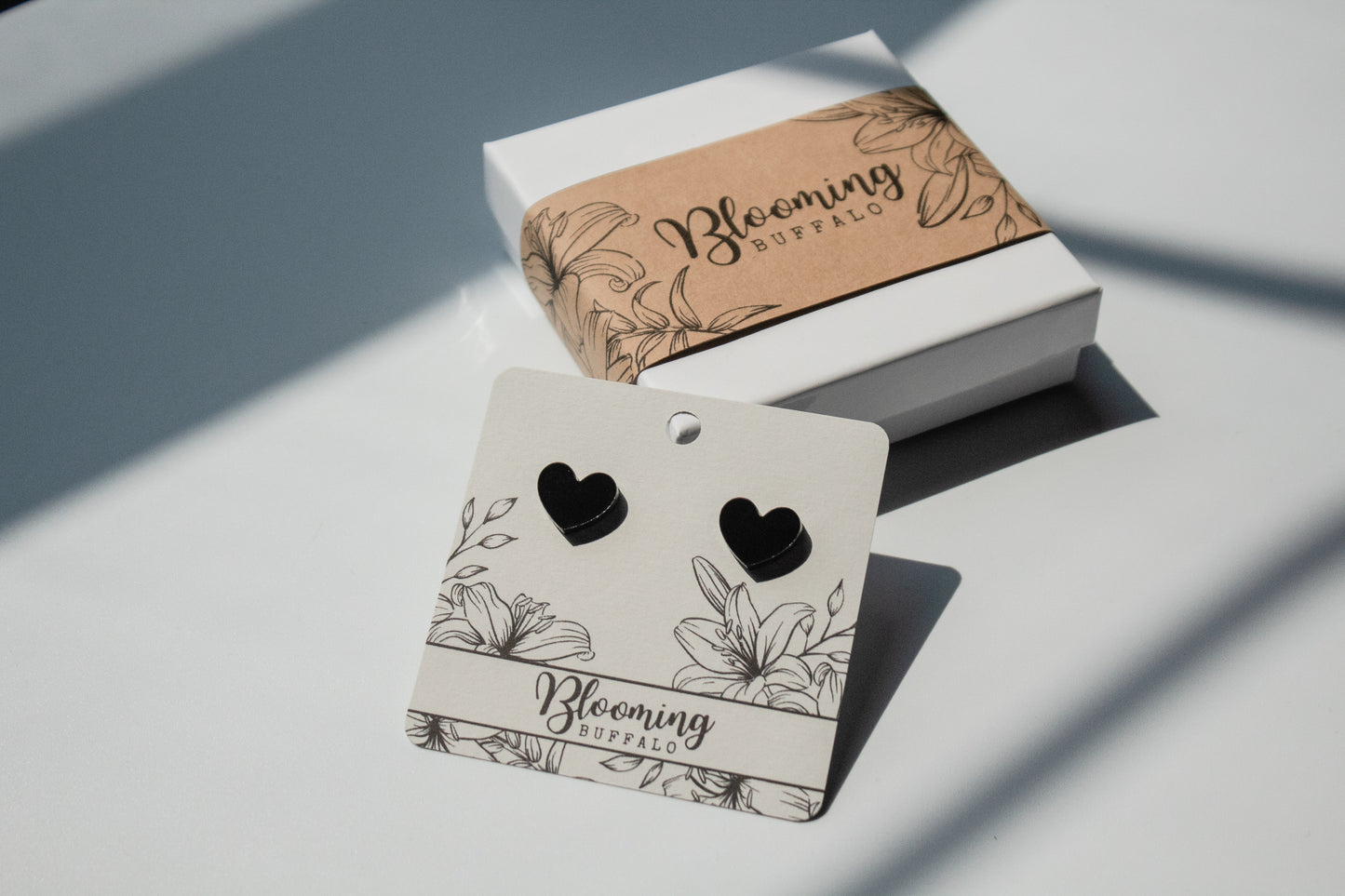 pure black heart shaped stud earrings on a Blooming Buffalo branded earring card resting on a Blooming Buffalo branded gift box