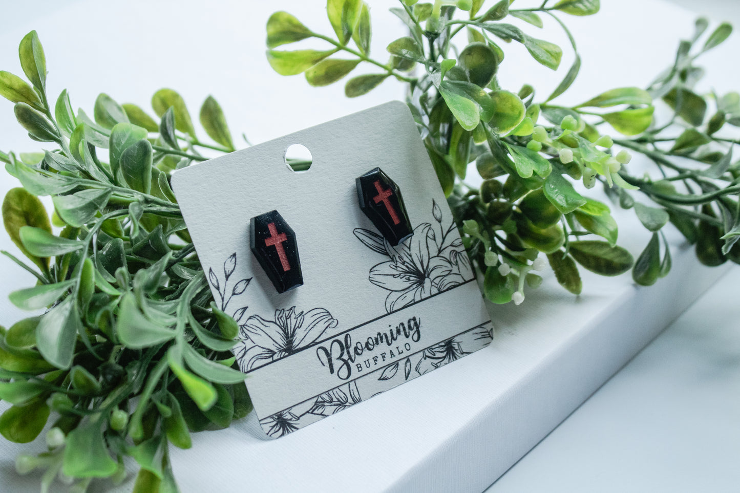 Black coffin stud earrings with red crosses on a Blooming Buffalo branded earring card