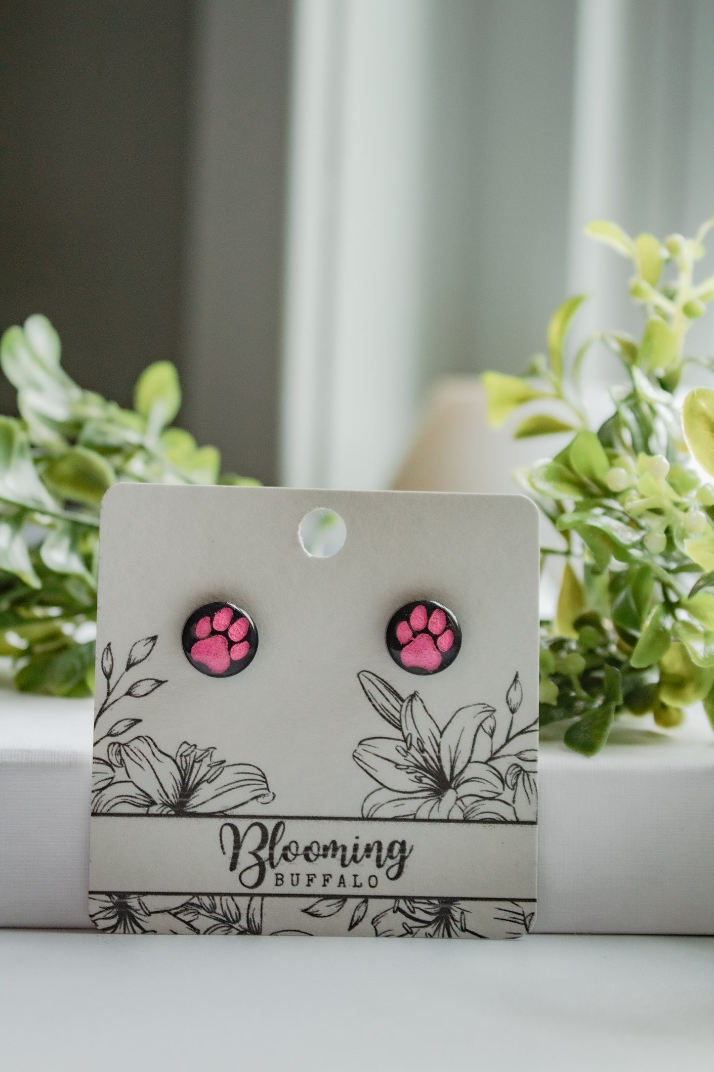black circular stud earrings with pink pawprints on Blooming Buffalo branded earring card