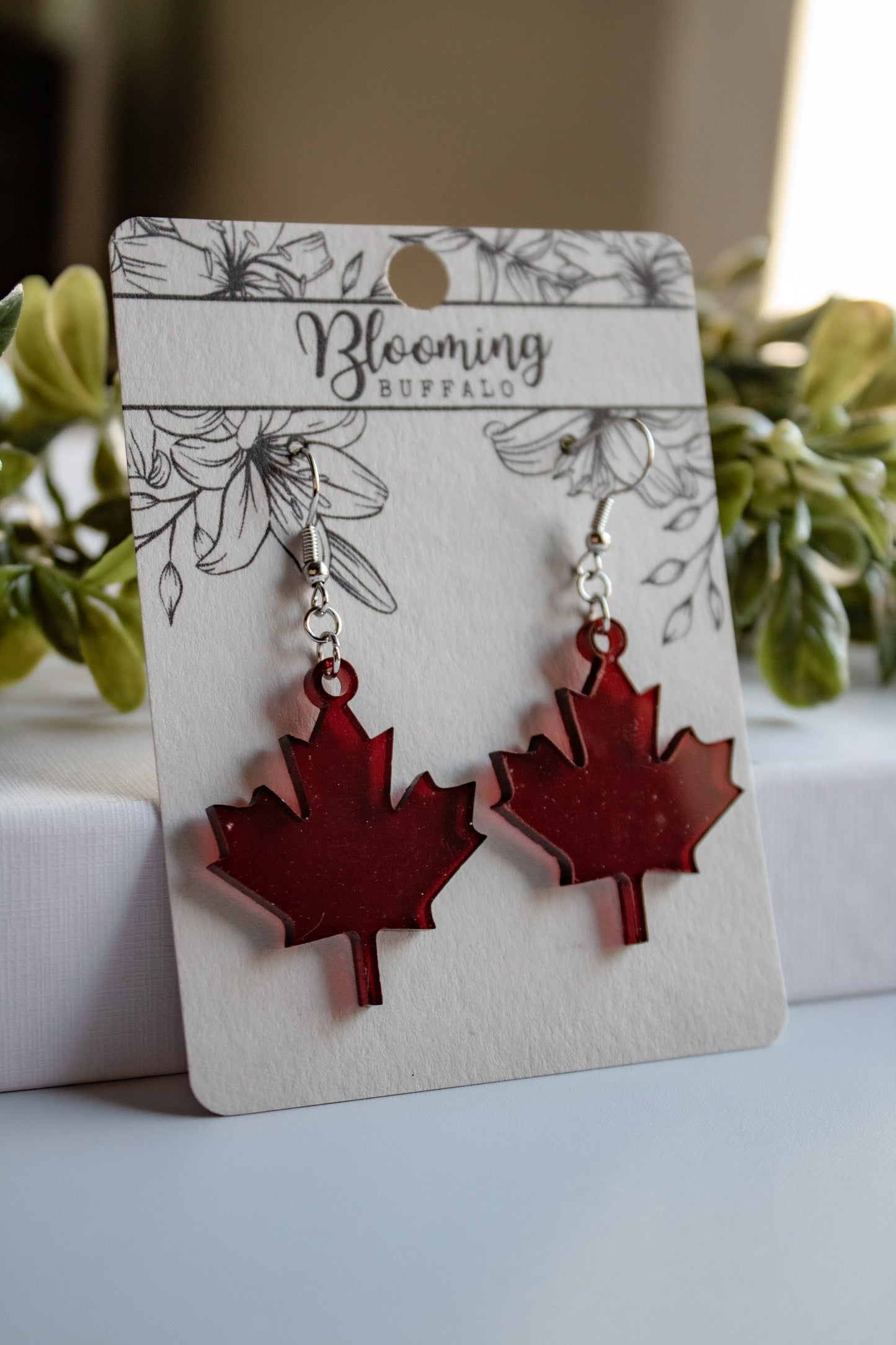 translucent dark red maple leaf dangle earrings on a Blooming Buffalo branded earring card