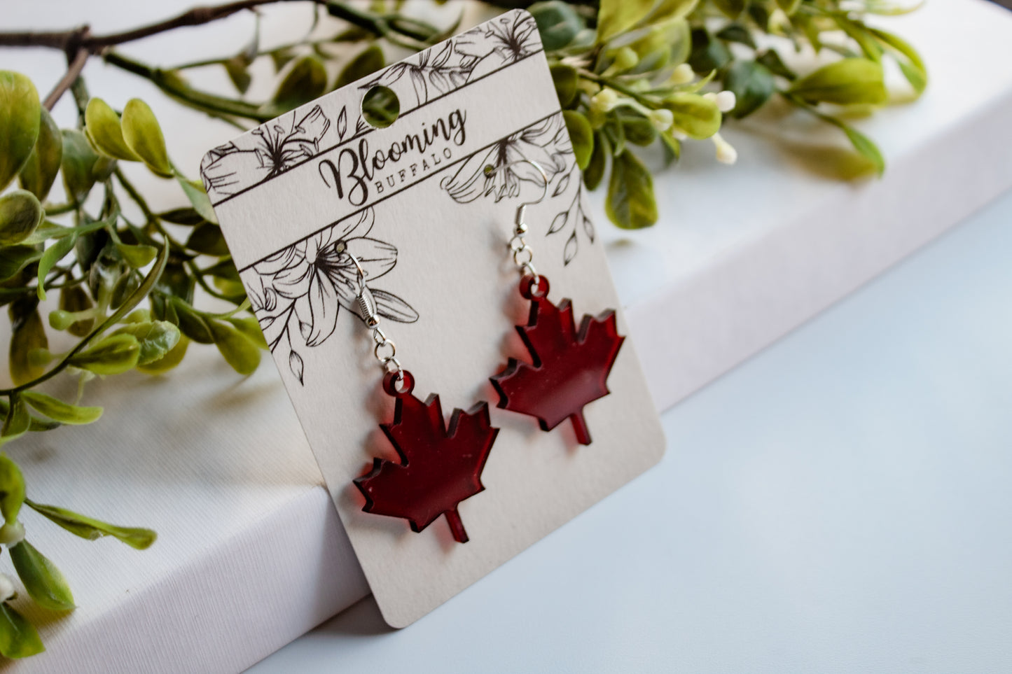 translucent dark red maple leaf dangle earrings on a Blooming Buffalo branded earring card