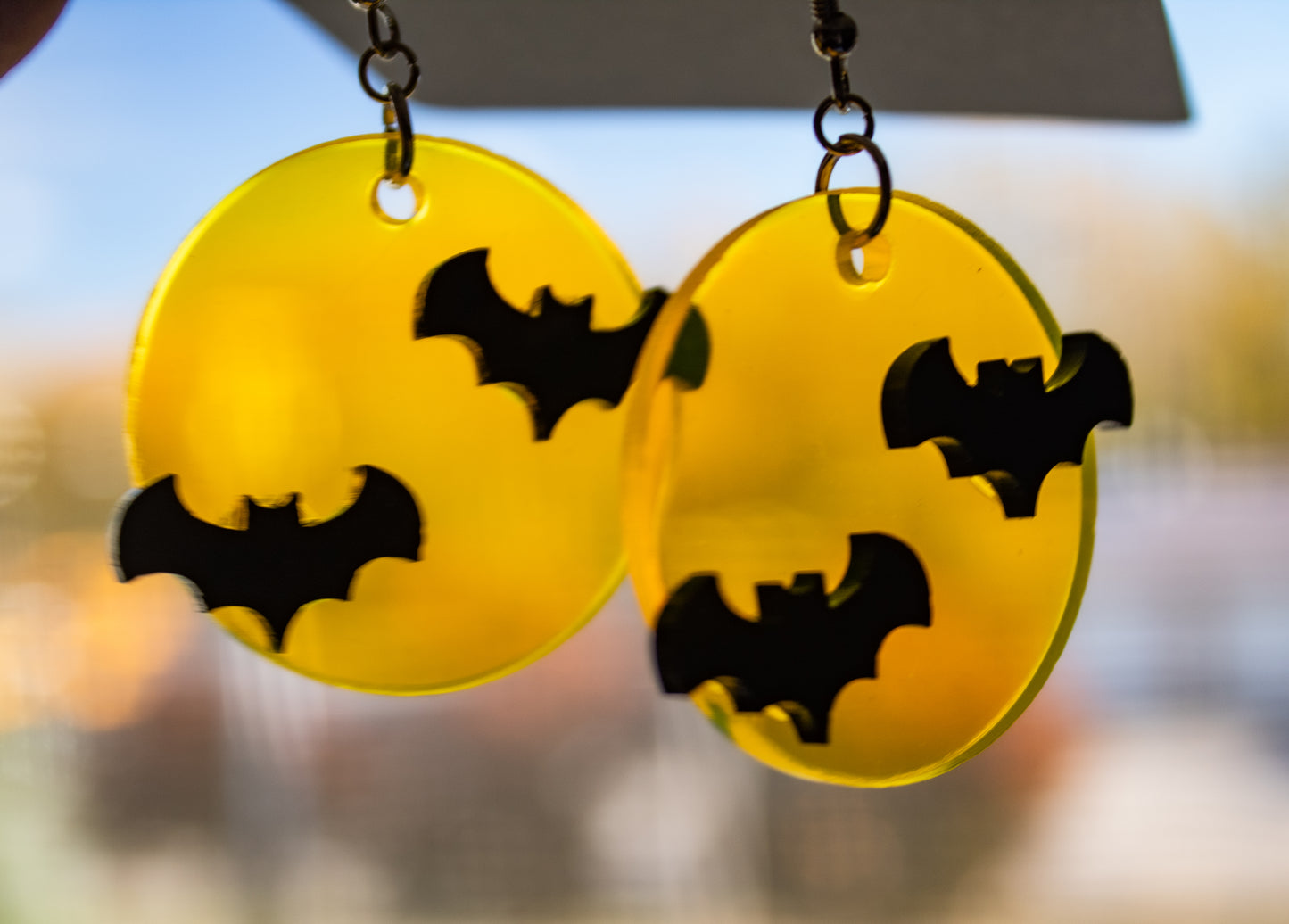 Translucent yellow full moon dangle earrings with two black bats on each earring. The earrings are held up to the light to show the bright, translucent design.