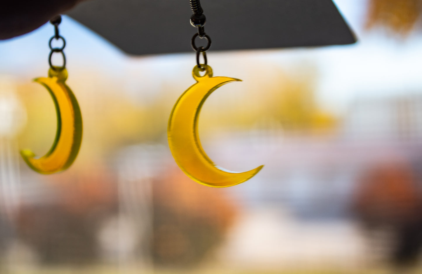 fluorescent yellow crescent moon dangle earrings in front of window to show light coming through