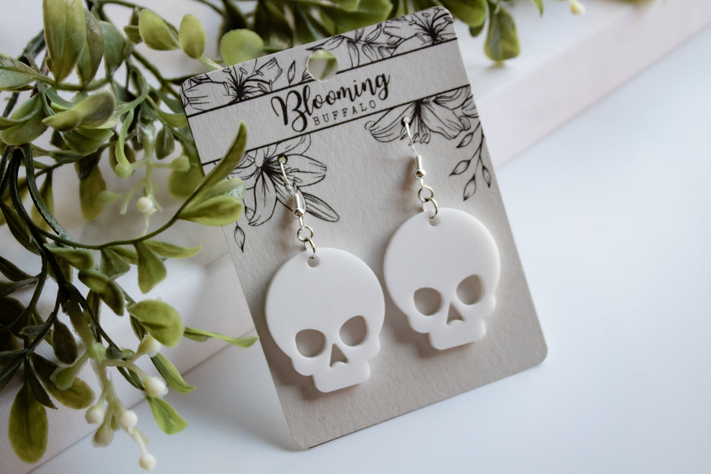 Large white skull dangle earrings on Blooming Buffalo branded earring card