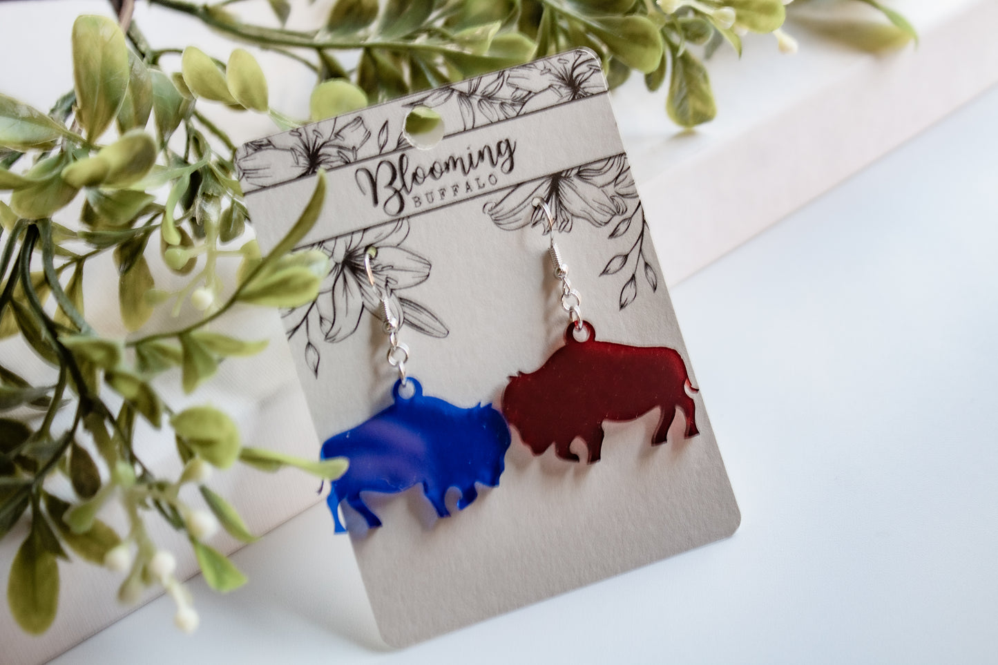 Translucent red and blue buffalo dangle earrings on a Blooming Buffalo branded earring card