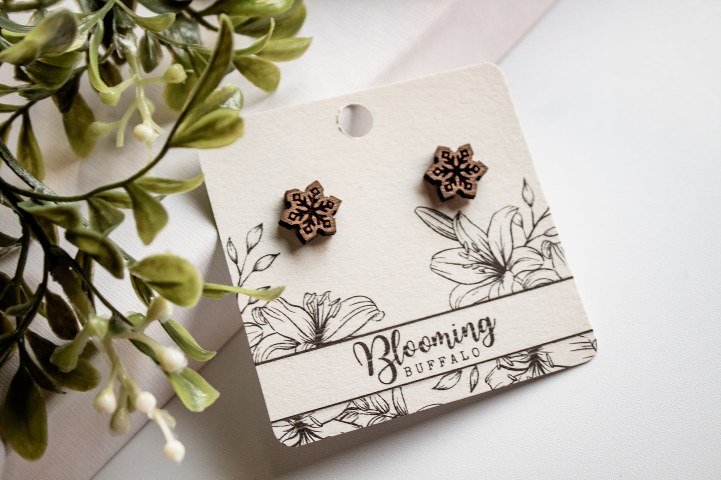 wooden snowflake stud earrings on a Blooming Buffalo branded earring card.