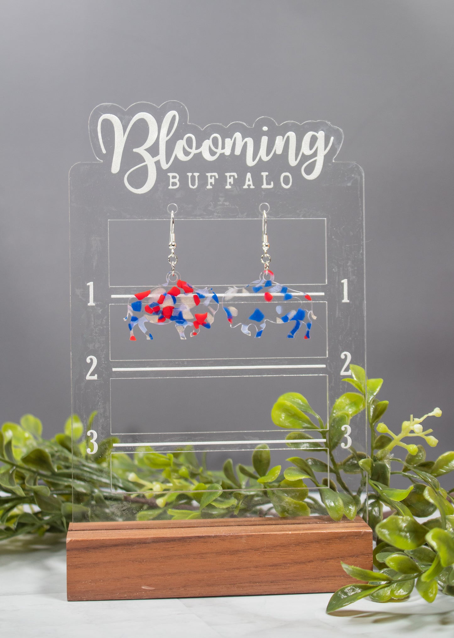 clear acrylic buffalo dangle earrings with red white and blue confetti in the acrylic. Earrings are on a Blooming Buffalo branded earring stand