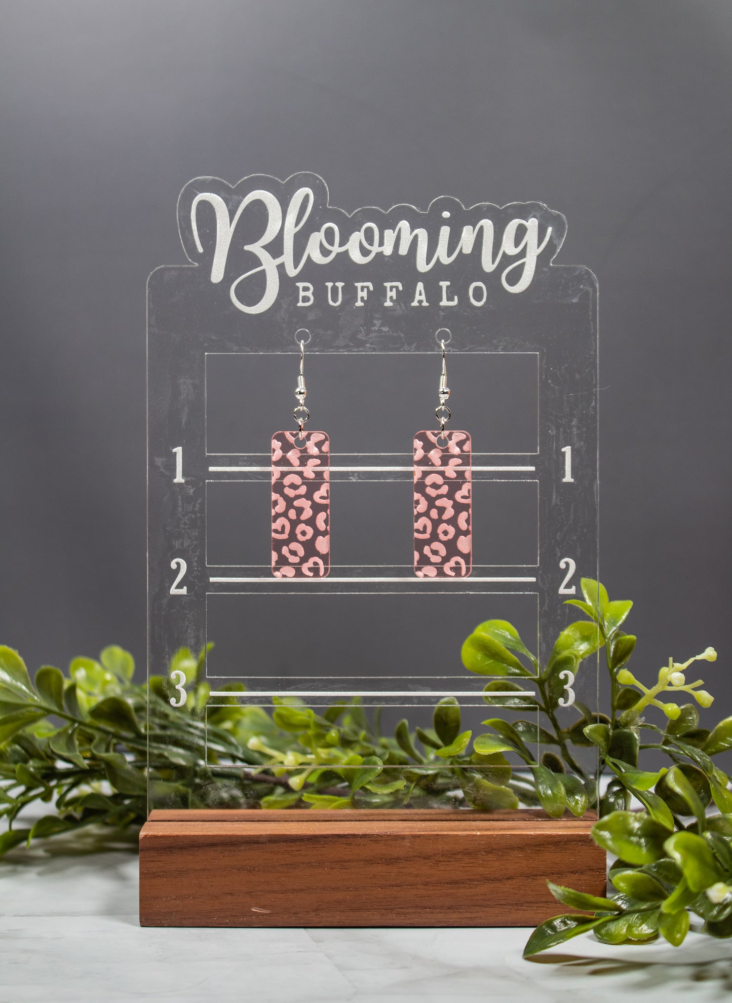 translucent rose gold rectangle acrylic earrings with heart shaped leopard print engraved on earrings. Earrings on a Blooming Buffalo branded earring stand