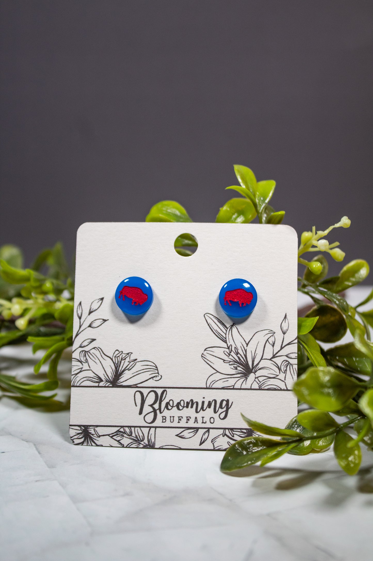vibrant blue circle stud earrings with a red buffalo design on a Blooming Buffalo branded earring card