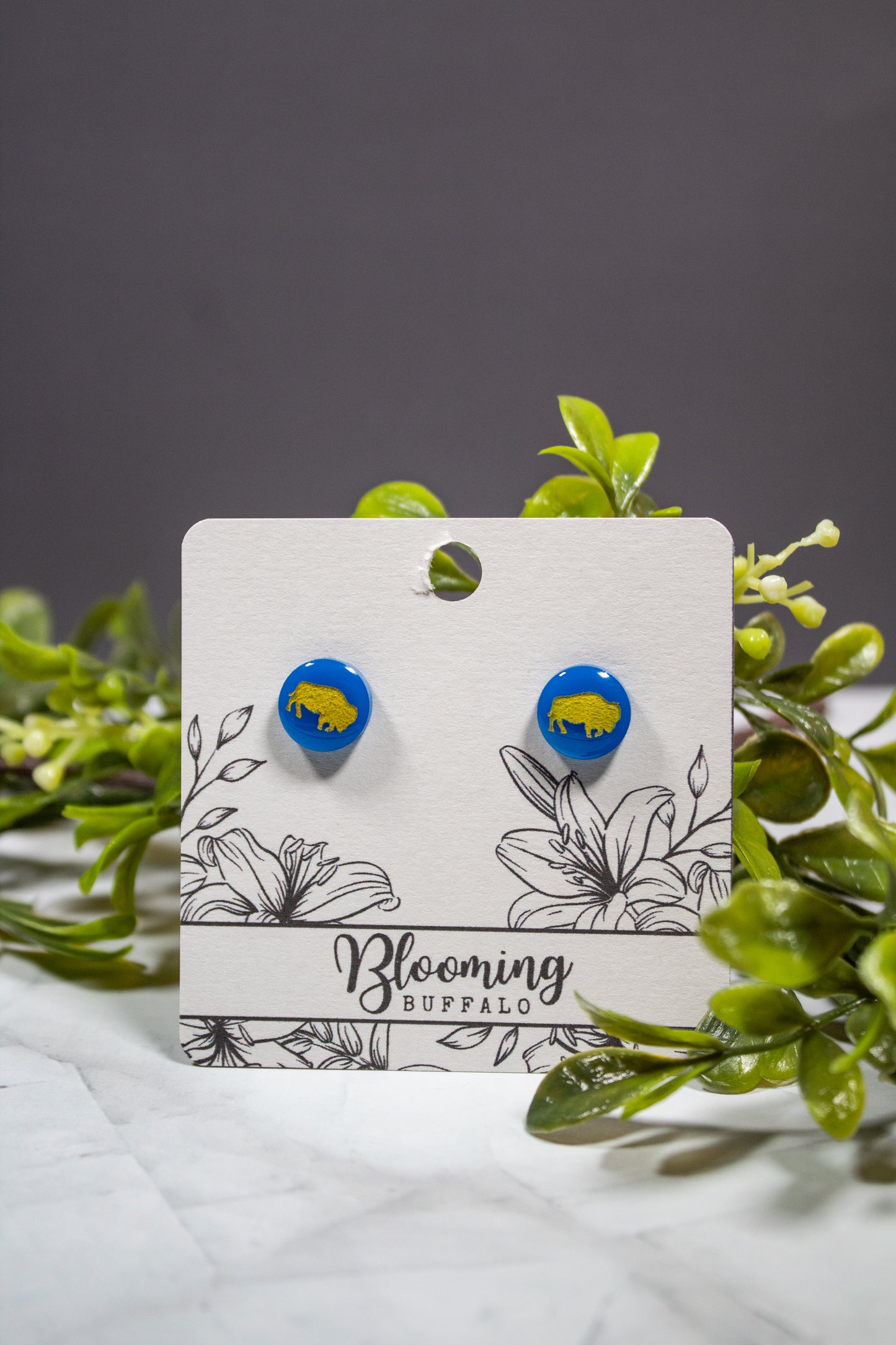 vibrant blue circle stud earrings with a yellow buffalo design on a Blooming Buffalo branded earring card