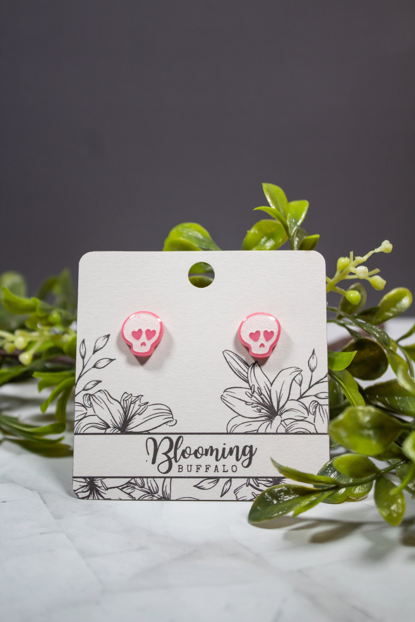 pink and white skull stud earrings with pink heart eyes on a Blooming Buffalo branded earring card