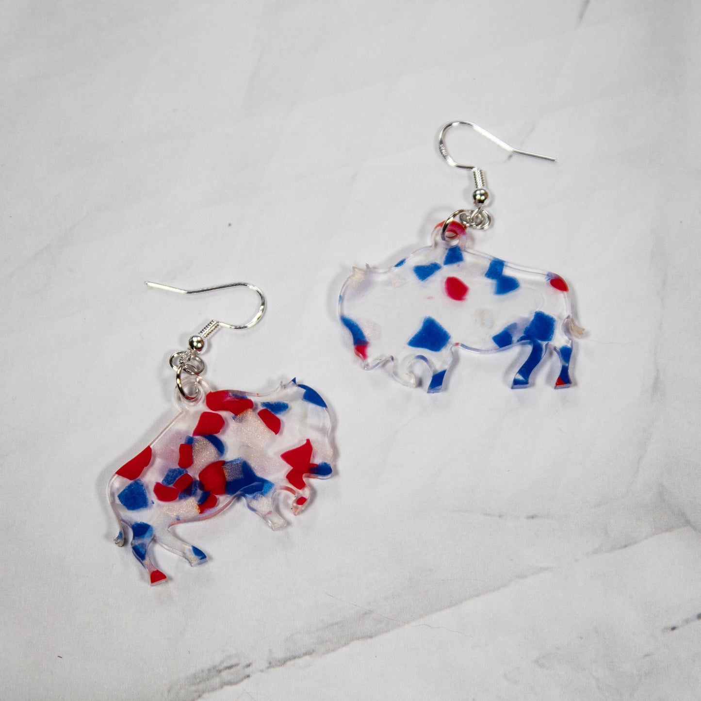 clear acrylic buffalo dangle earrings with red white and blue confetti in the acrylic. Earrings are on a white marbled background