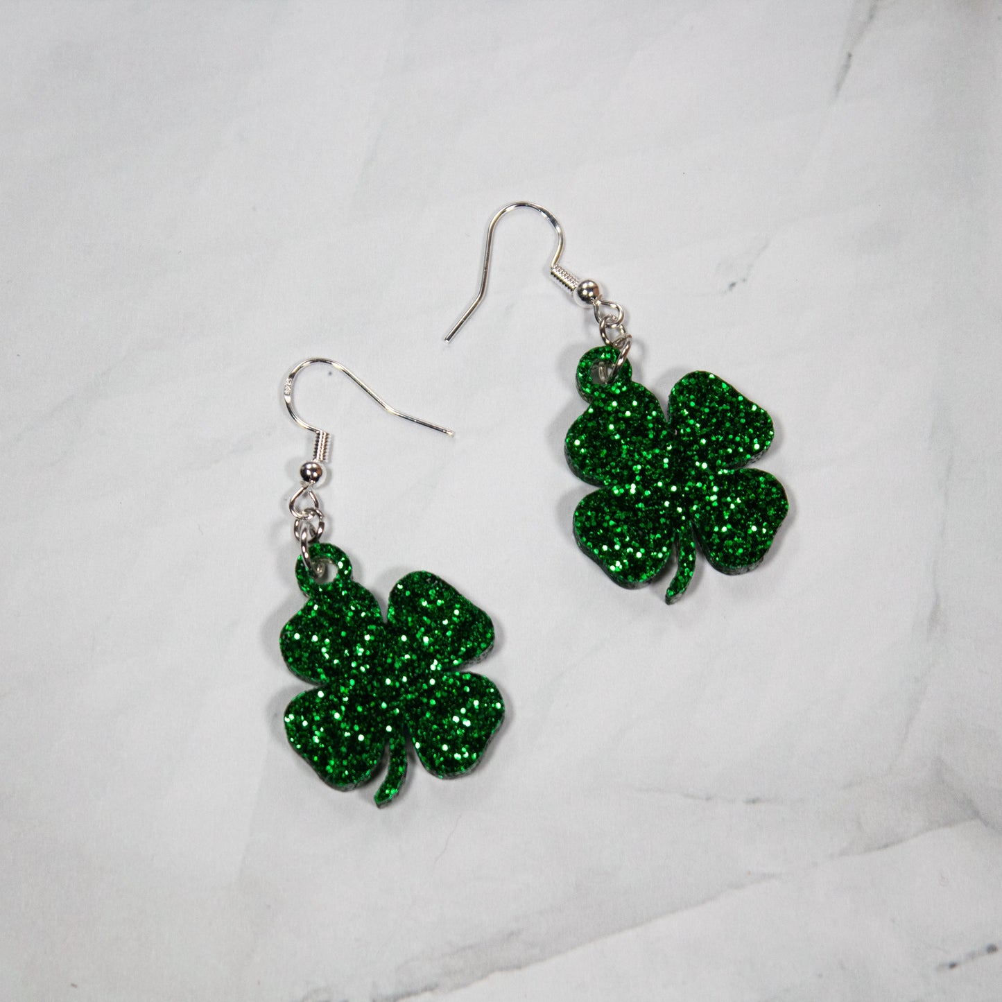 sparkling green glitter four-leaf clover shamrock dangle earrings on white marble background