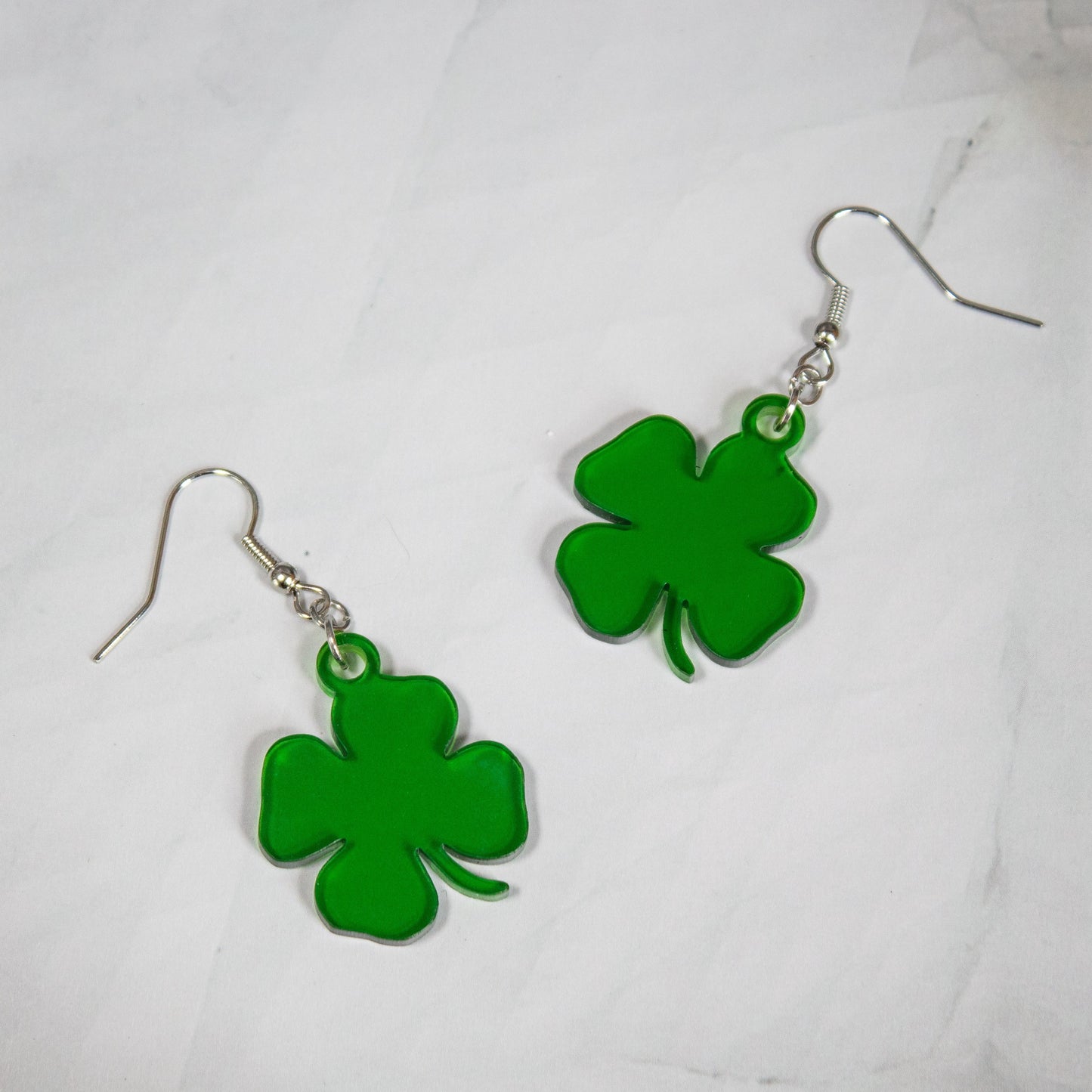 translucent green four-leaf clover shamrock dangle earrings on white marble background