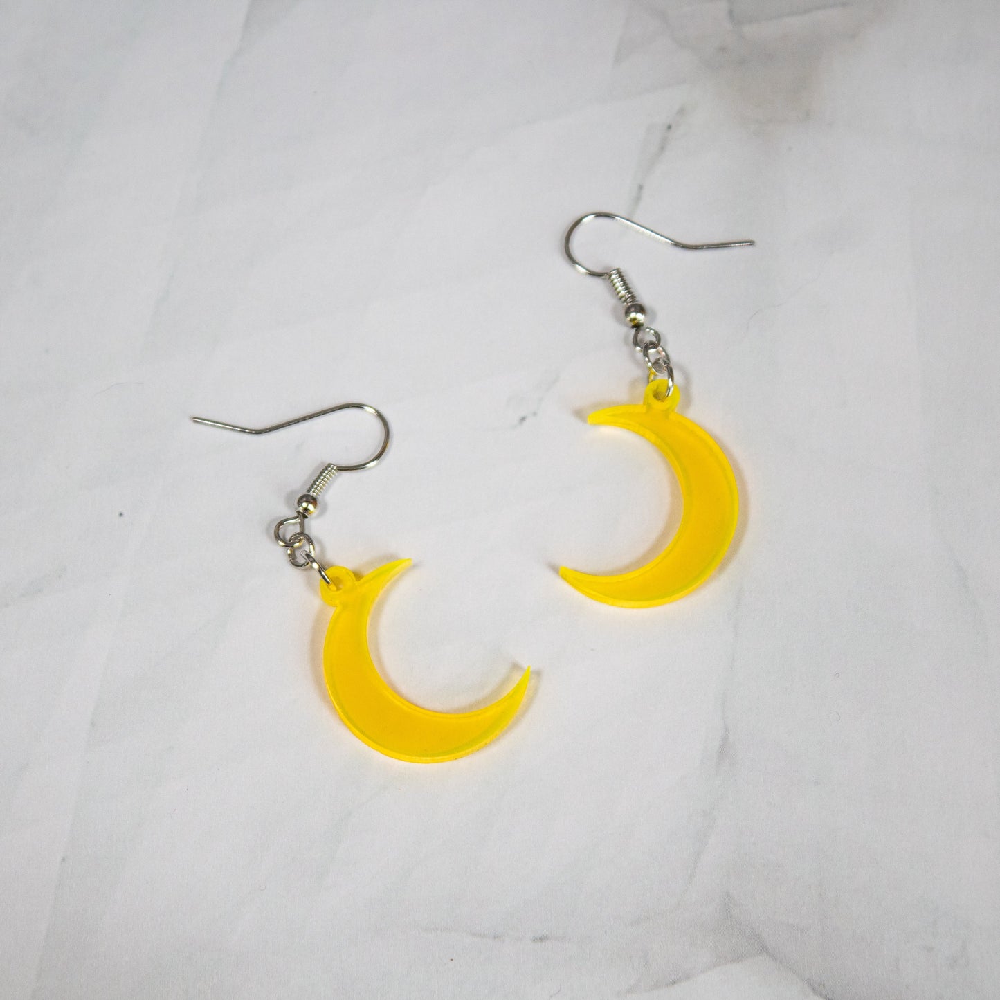 fluorescent yellow crescent moon dangle earrings on white marble background