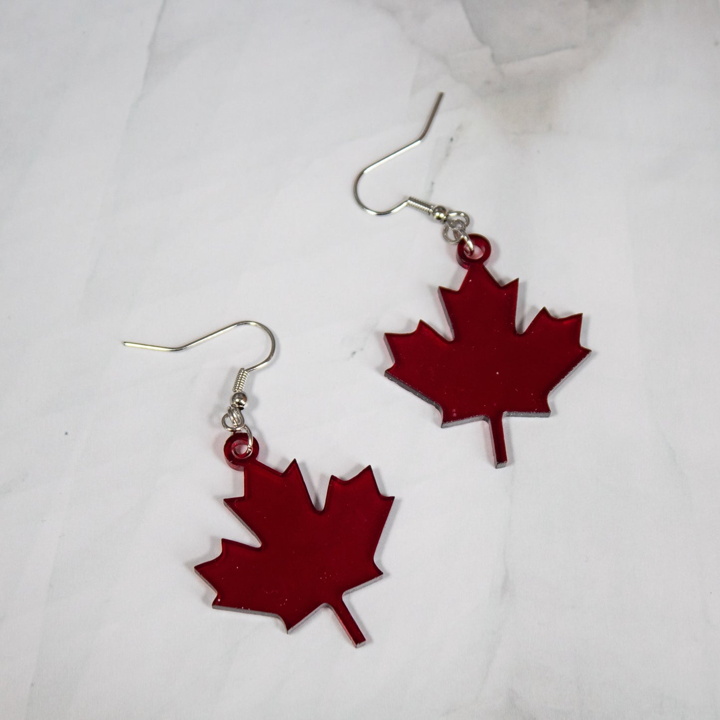 translucent dark red maple leaf dangle earrings on a white marble background