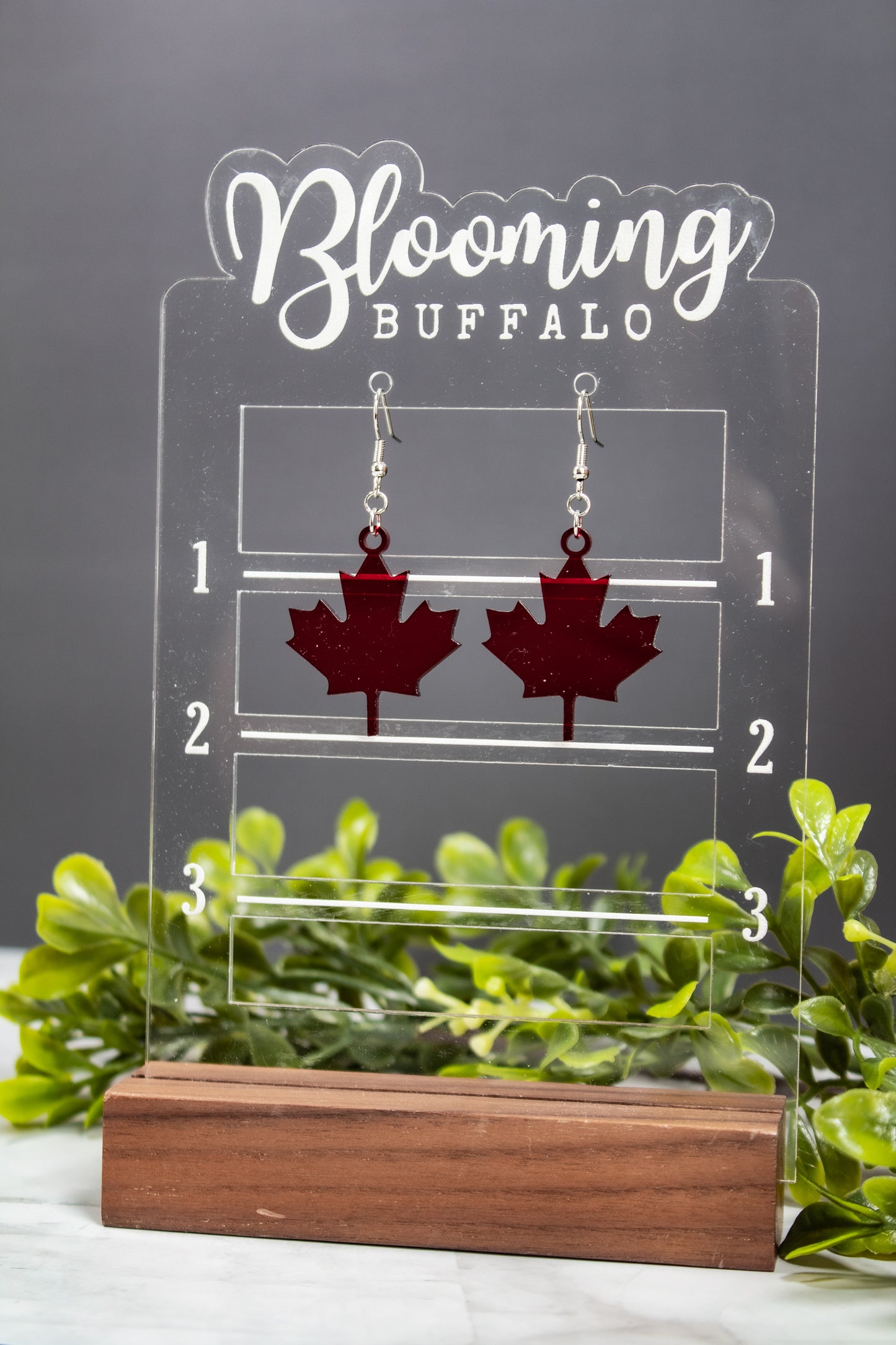 translucent dark red maple leaf dangle earrings on a Blooming Buffalo branded earring display stand