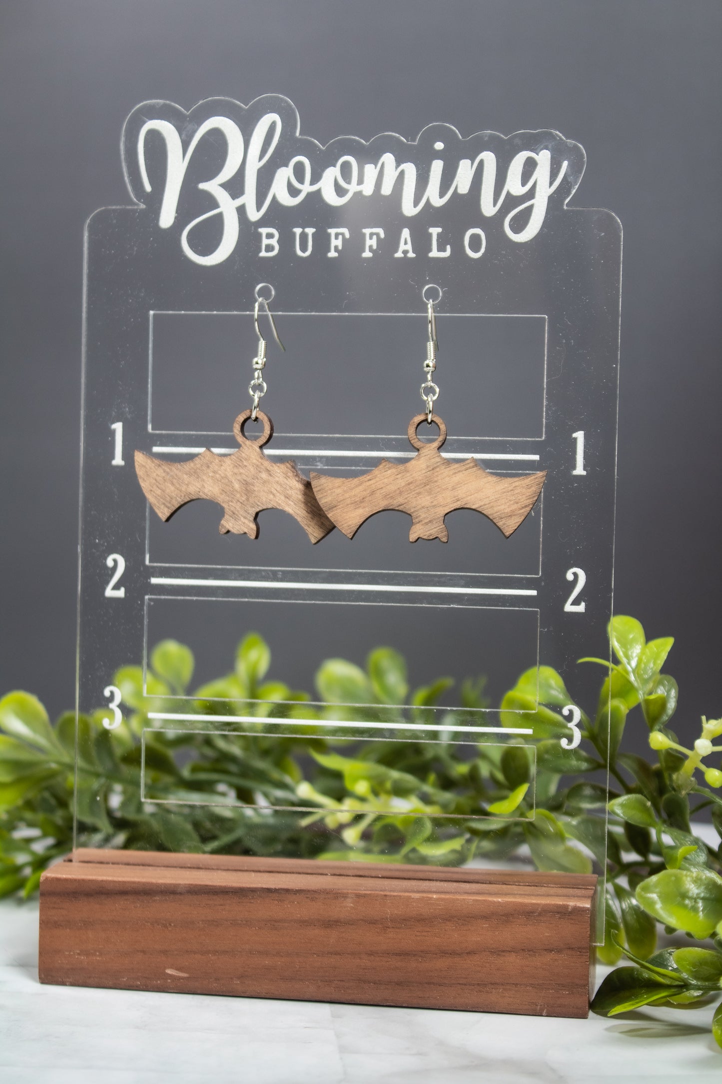 Spooky Halloween medium toned wood bat dangle earrings on Blooming Buffalo branded earring stand