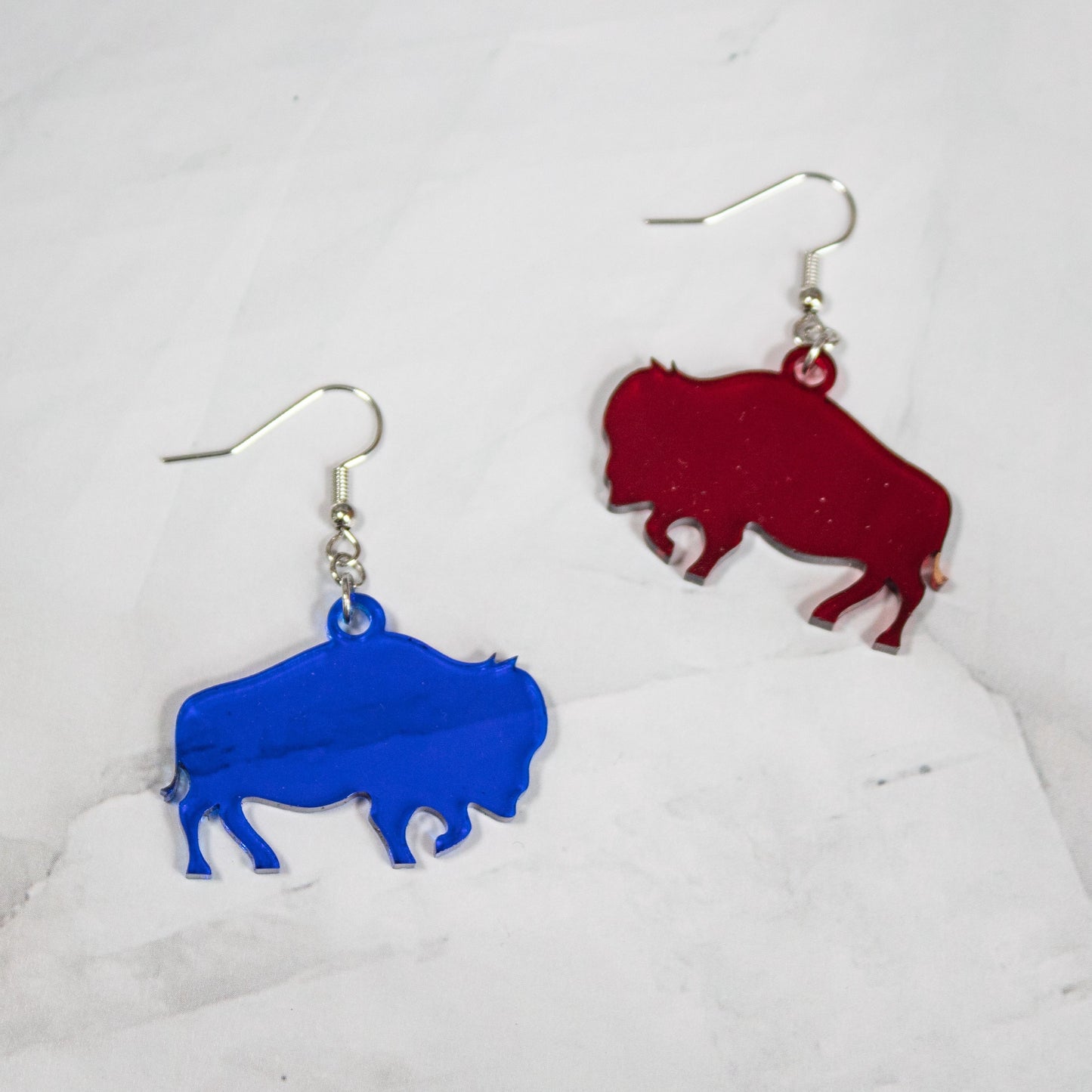 Translucent red and blue buffalo dangle earrings on a white marble background