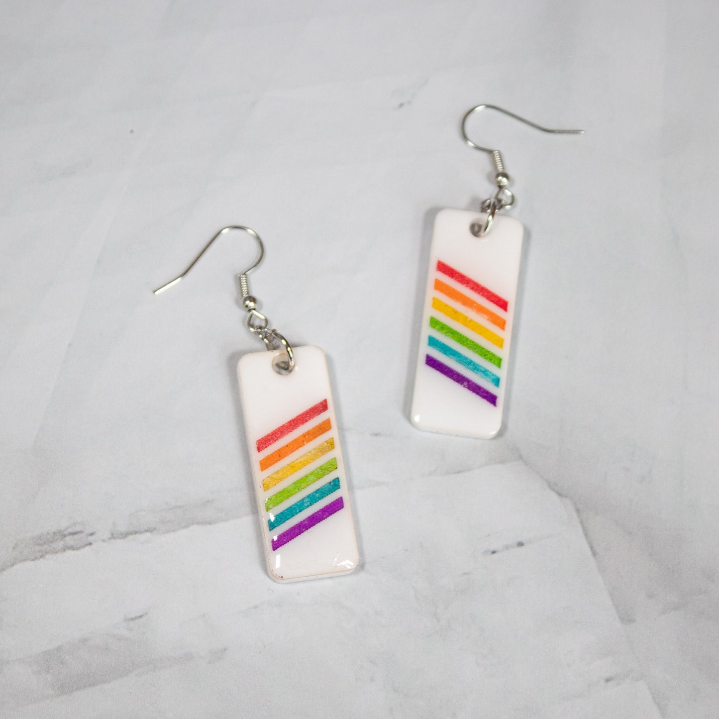 white rectangle dangle earrings with rainbow stripes on a white marble background