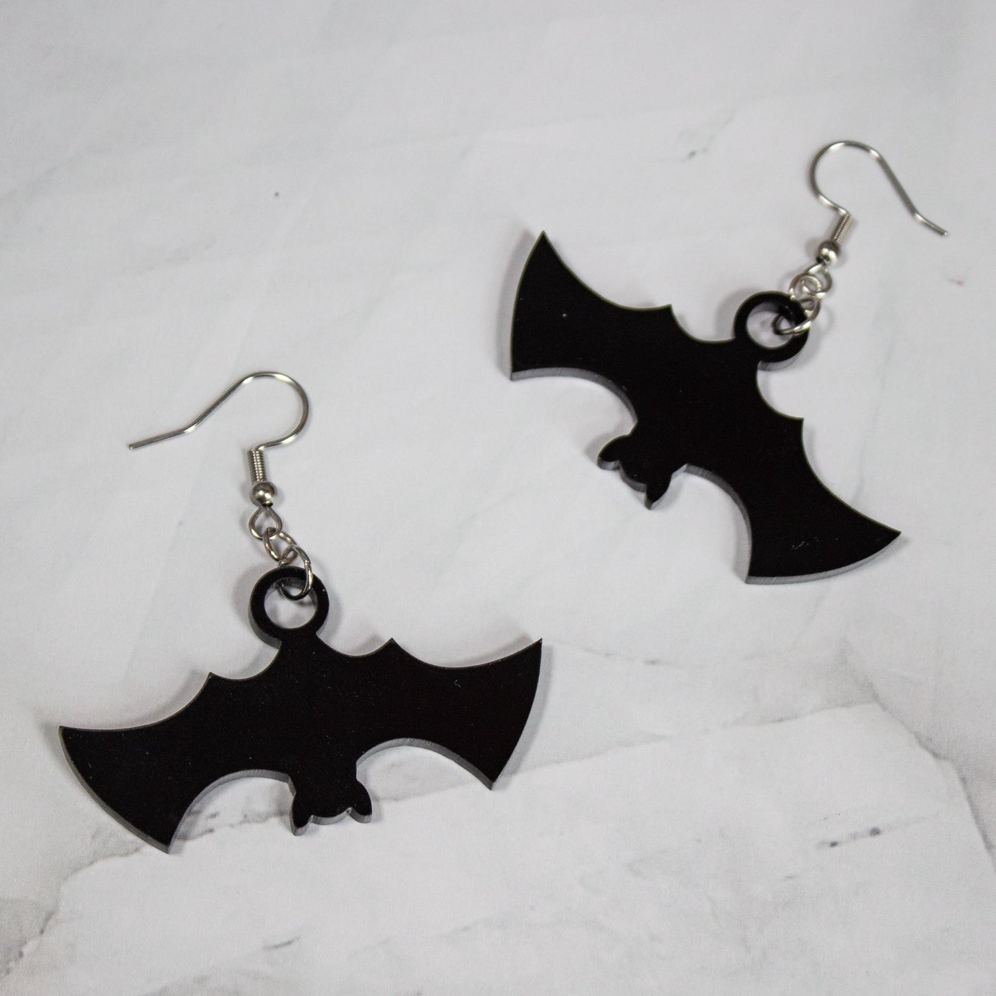 Spooky Halloween black bat dangle earrings on white marble background