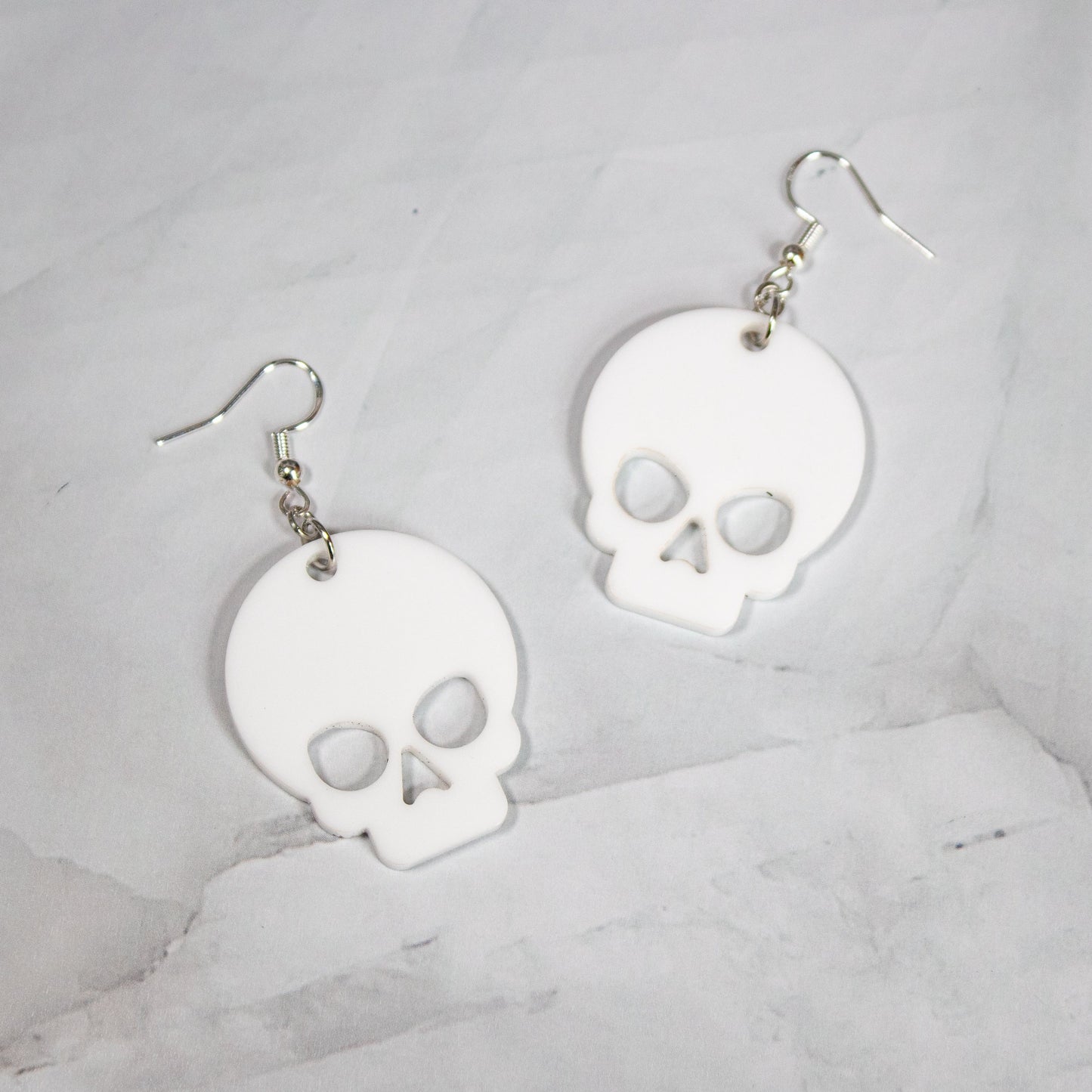 Large white skull dangle earrings on white marble background