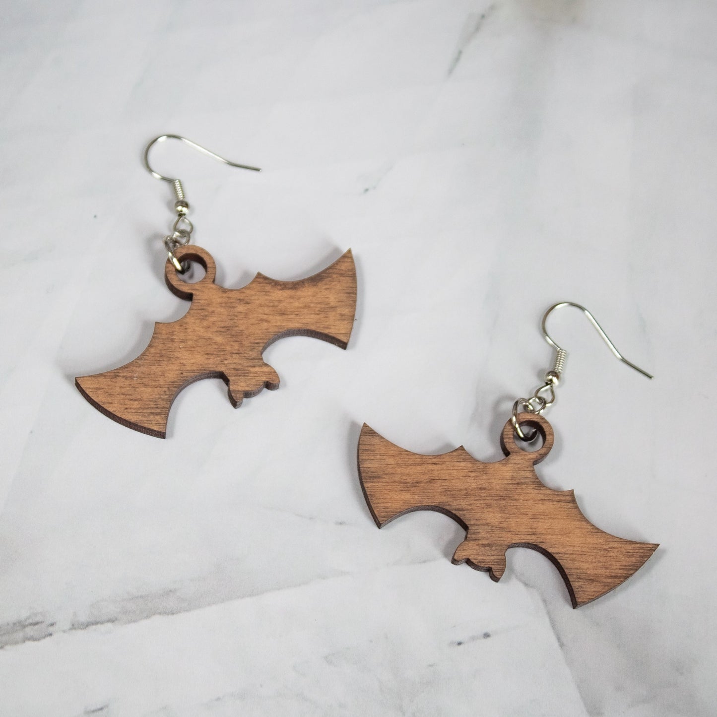 Spooky Halloween medium toned wood bat dangle earrings on white marble background