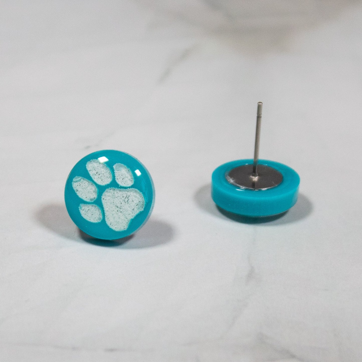 teal circle stud earrings with white paw print design on white marbled background