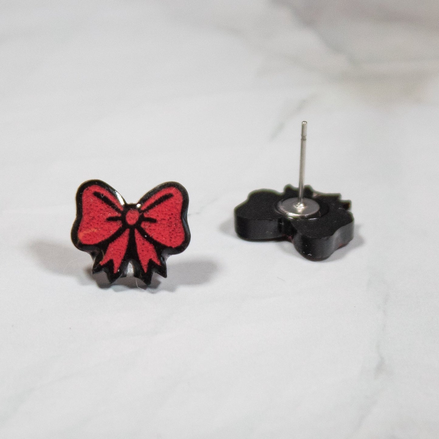 red and black gift bow stud earrings on white marble background