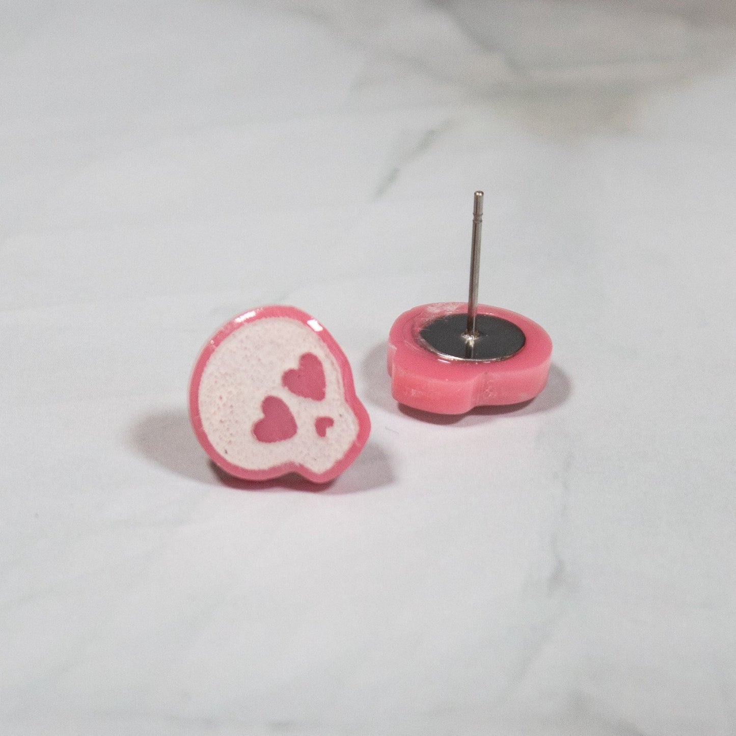 pink and white skull stud earrings with pink heart eyes on a white marbled background