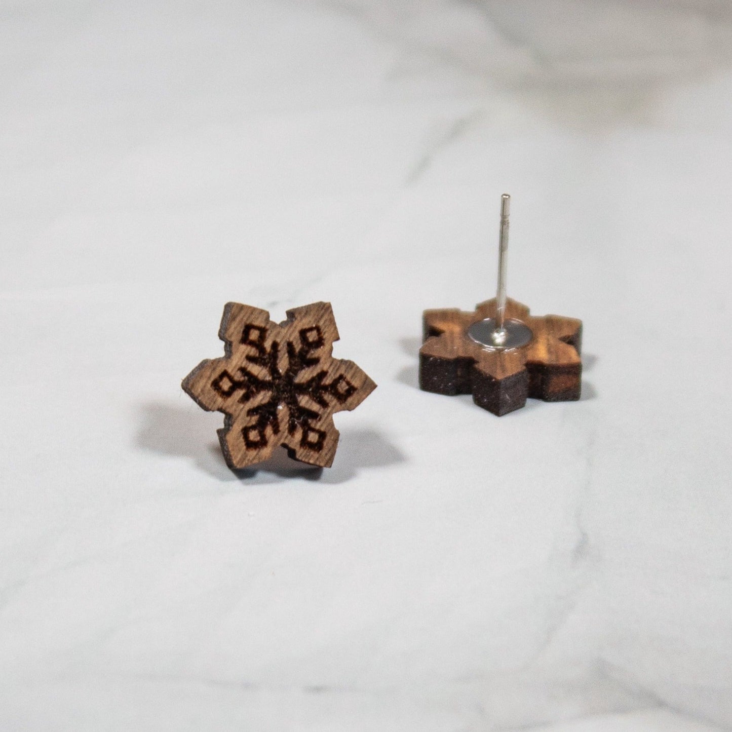 medium toned wooden snowflake stud earrings on a white marble background