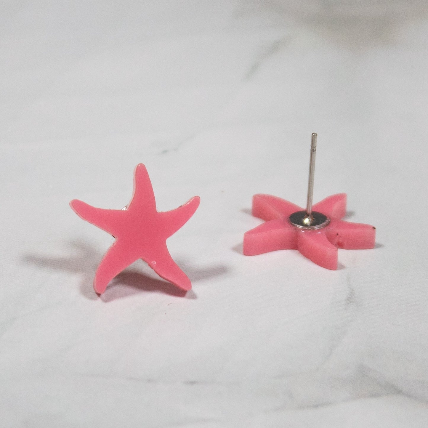 vibrant summery pink starfish style stud earrings on white marble background