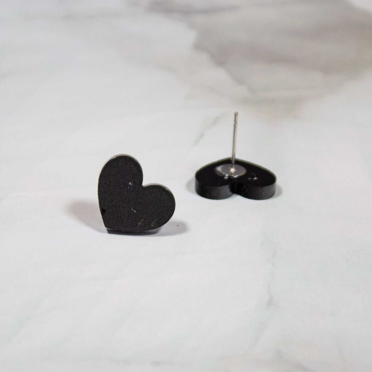 Black heart shaped stud earrings on a white marbled background