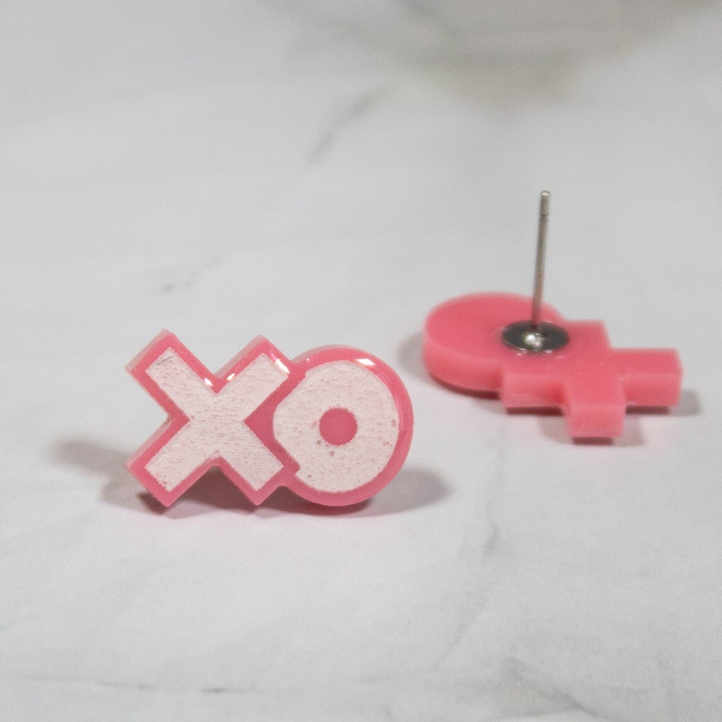 pink and white XO stud earrings on white marble background