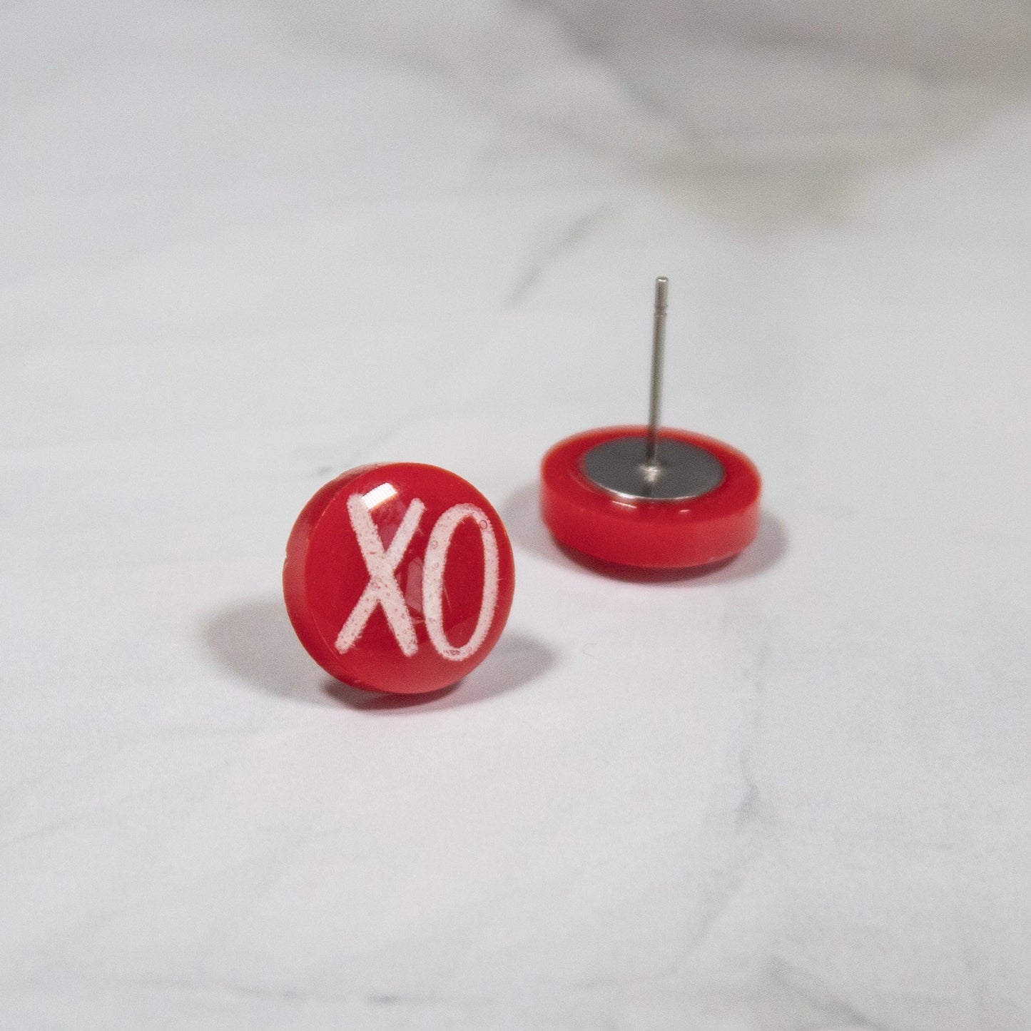 red circle stud earrings with a white XO design on a marbled white background