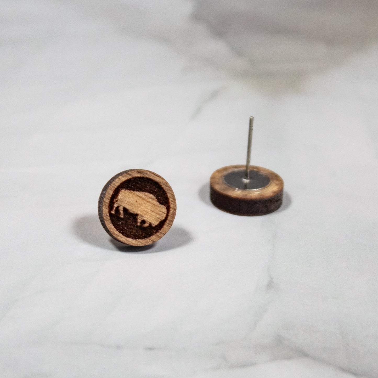 medium toned wood circle stud earrings with a buffalo design on a white marbled background