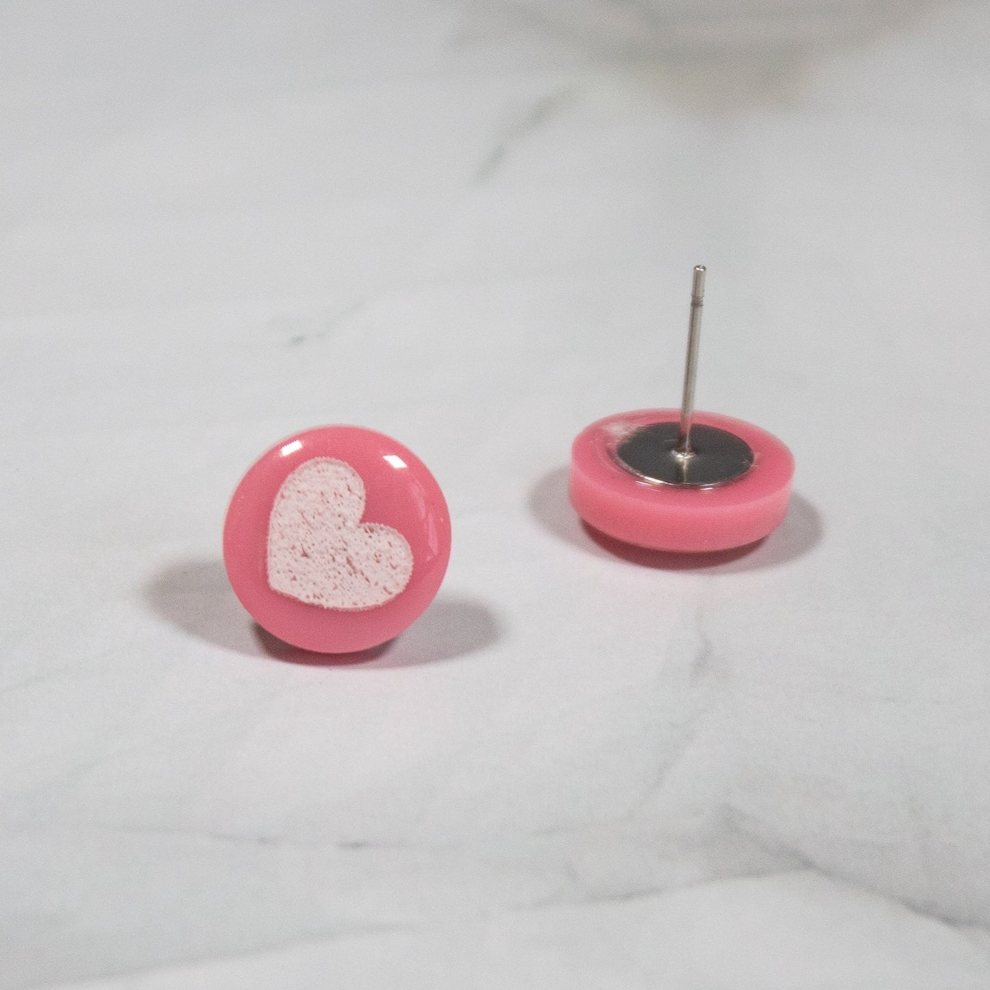 pink circle stud earrings with white heart design on white marble background