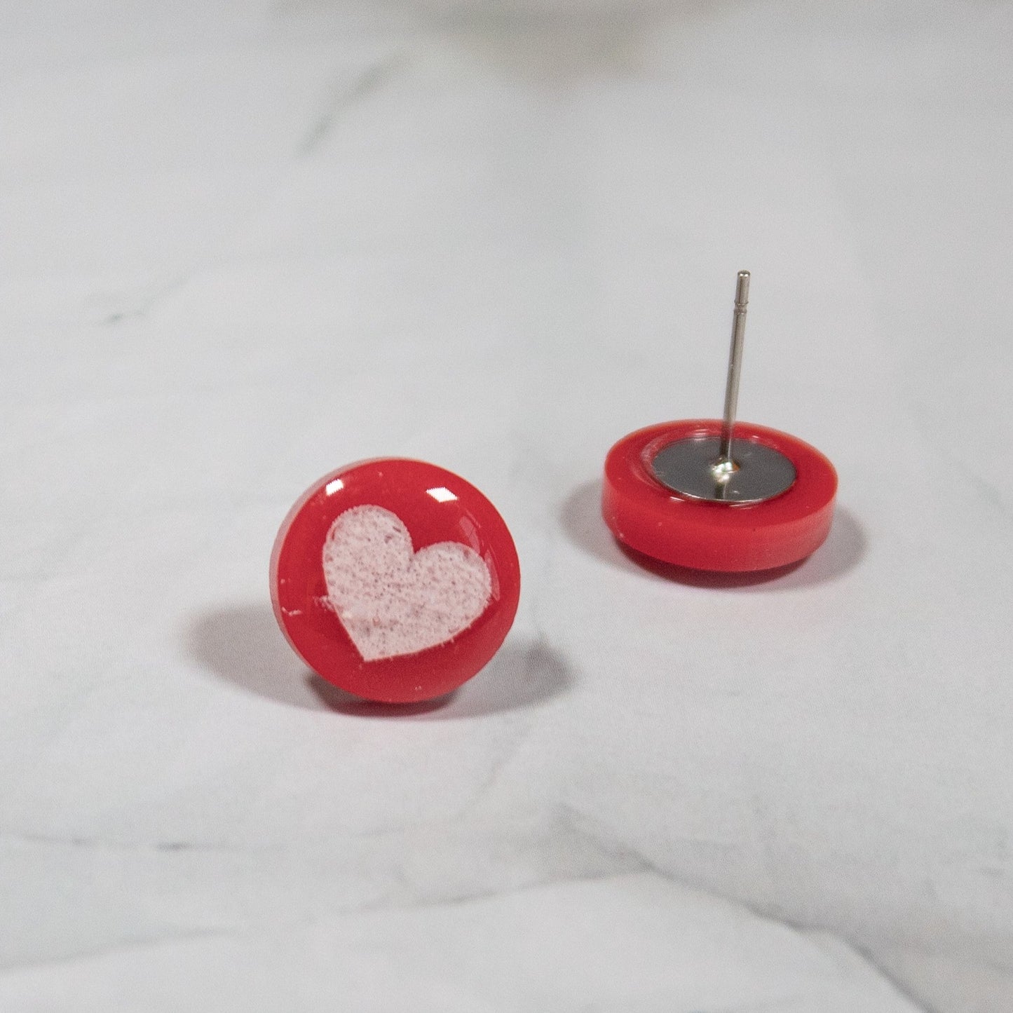 red circle stud earrings with white heart design on white marbled background
