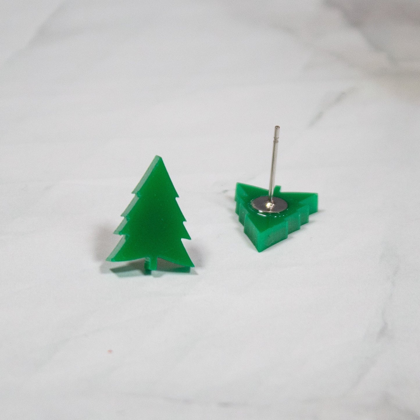 vibrant green evergreen tree shaped stud earrings on white marble background