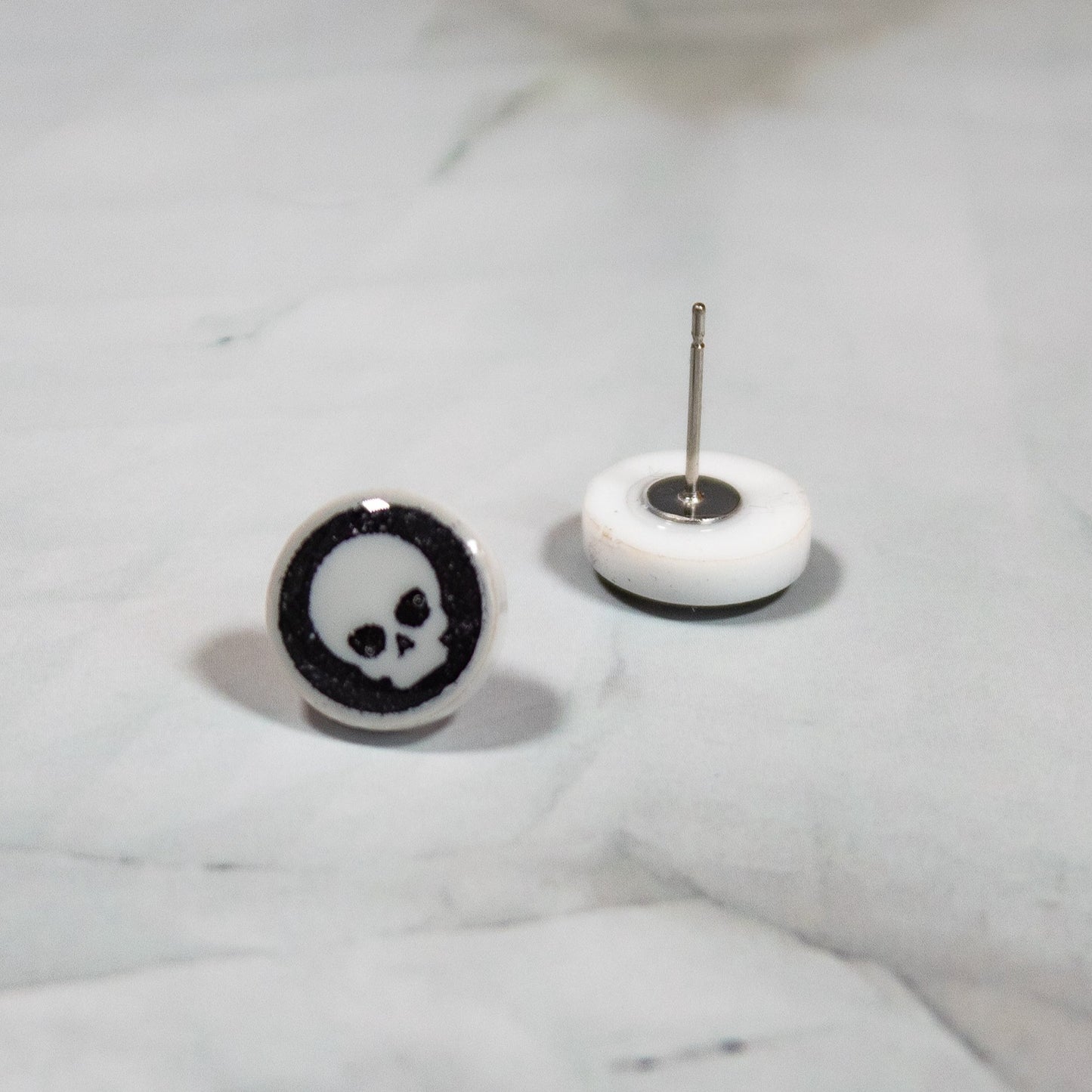 white circle stud earrings with a black background and white skull design resting on a white marbled background
