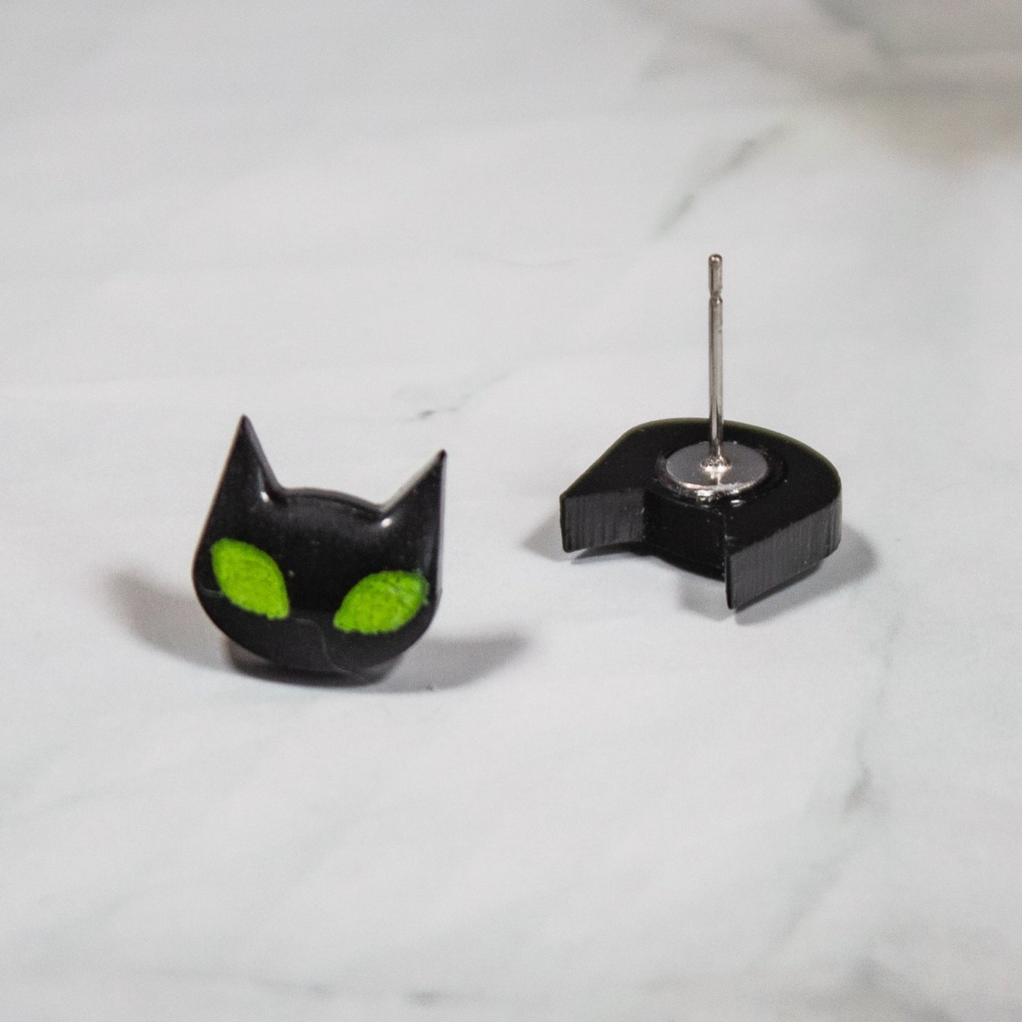 spooky black cat stud earrings with vibrant green eyes on white marble background
