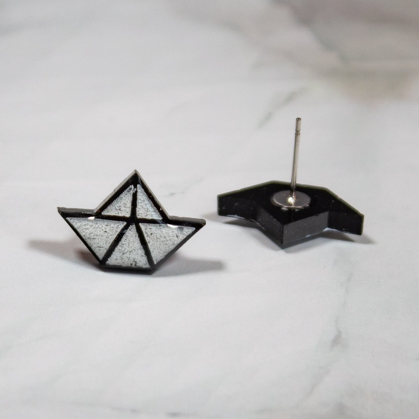 black and white origami paper boat stud earrings on white marbled background