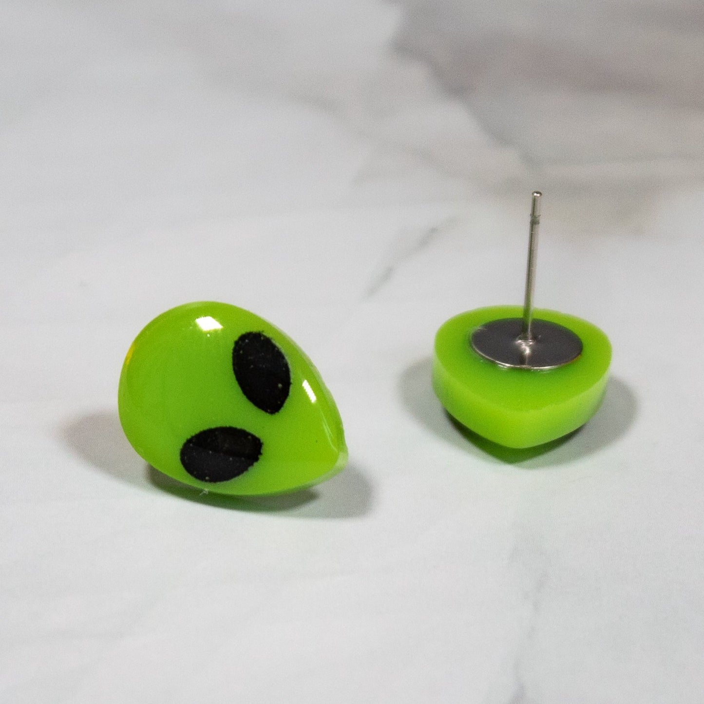 vibrant neon green alien stud earrings with black eyes on a white marble background