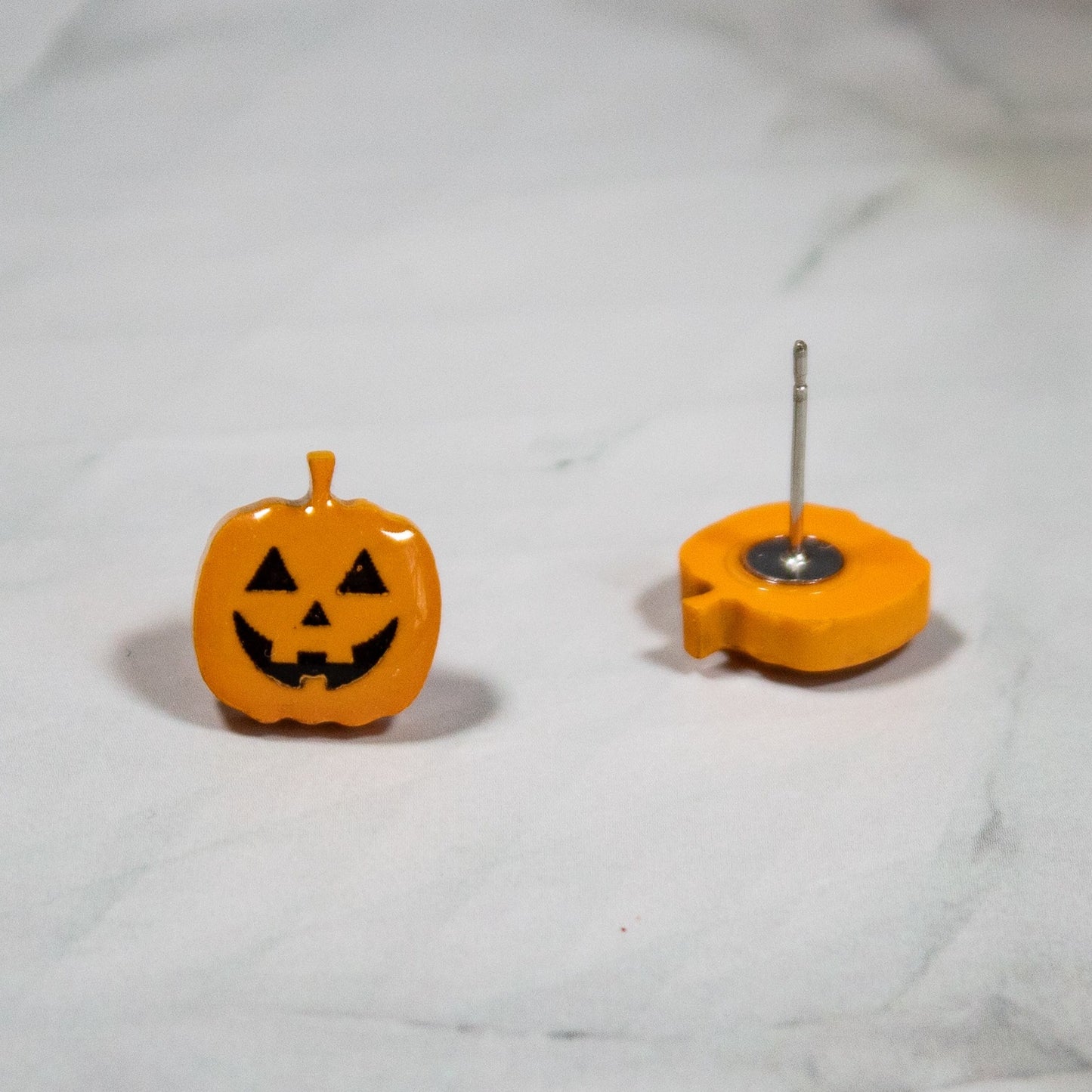 orange and black spooky jack-o-lantern halloween stud earrings on white marble background