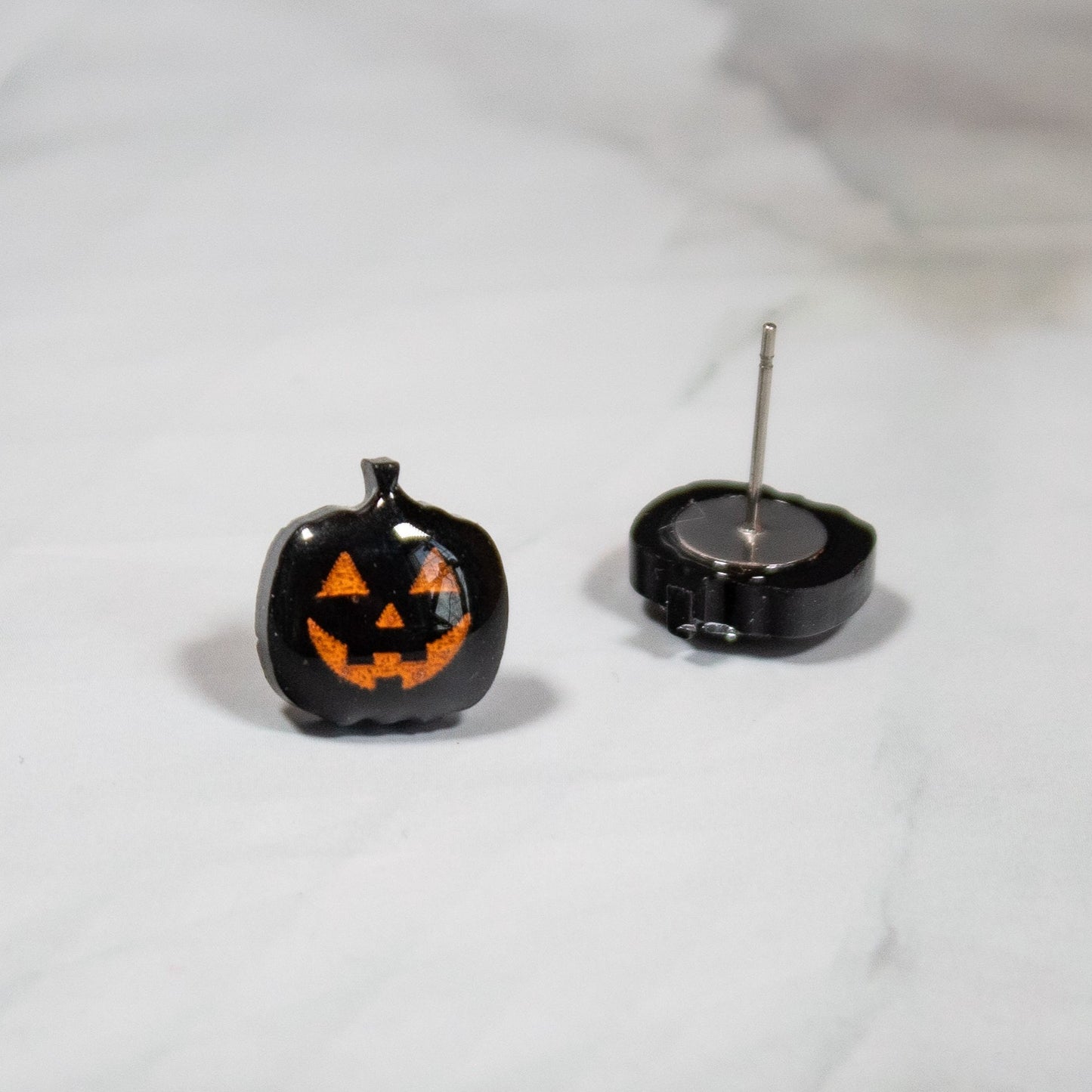 black and orange spooky jack-o-lantern halloween stud earrings on white marble background