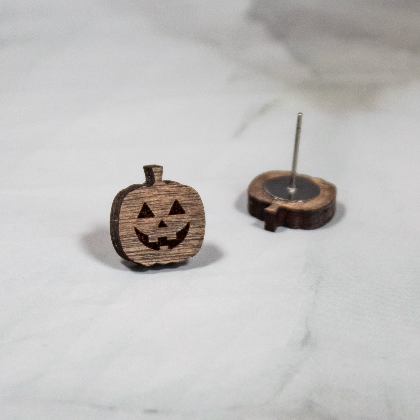 Medium toned wood spooky jack-o-lantern halloween stud earrings on white marble background