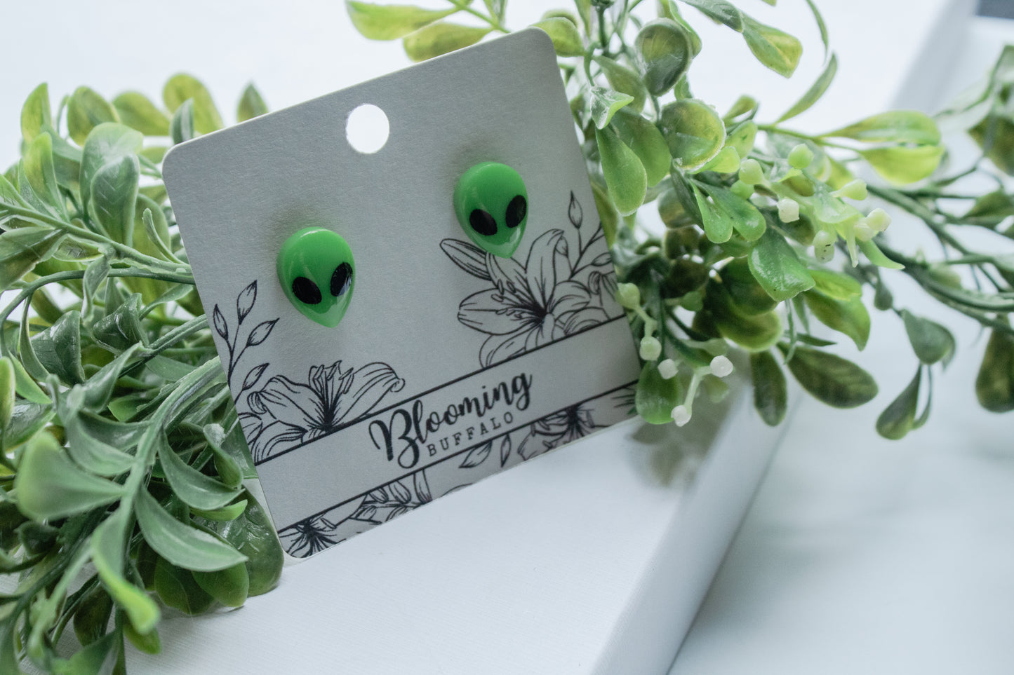 vibrant neon green alien stud earrings with black eyes on a Blooming Buffalo branded earring card